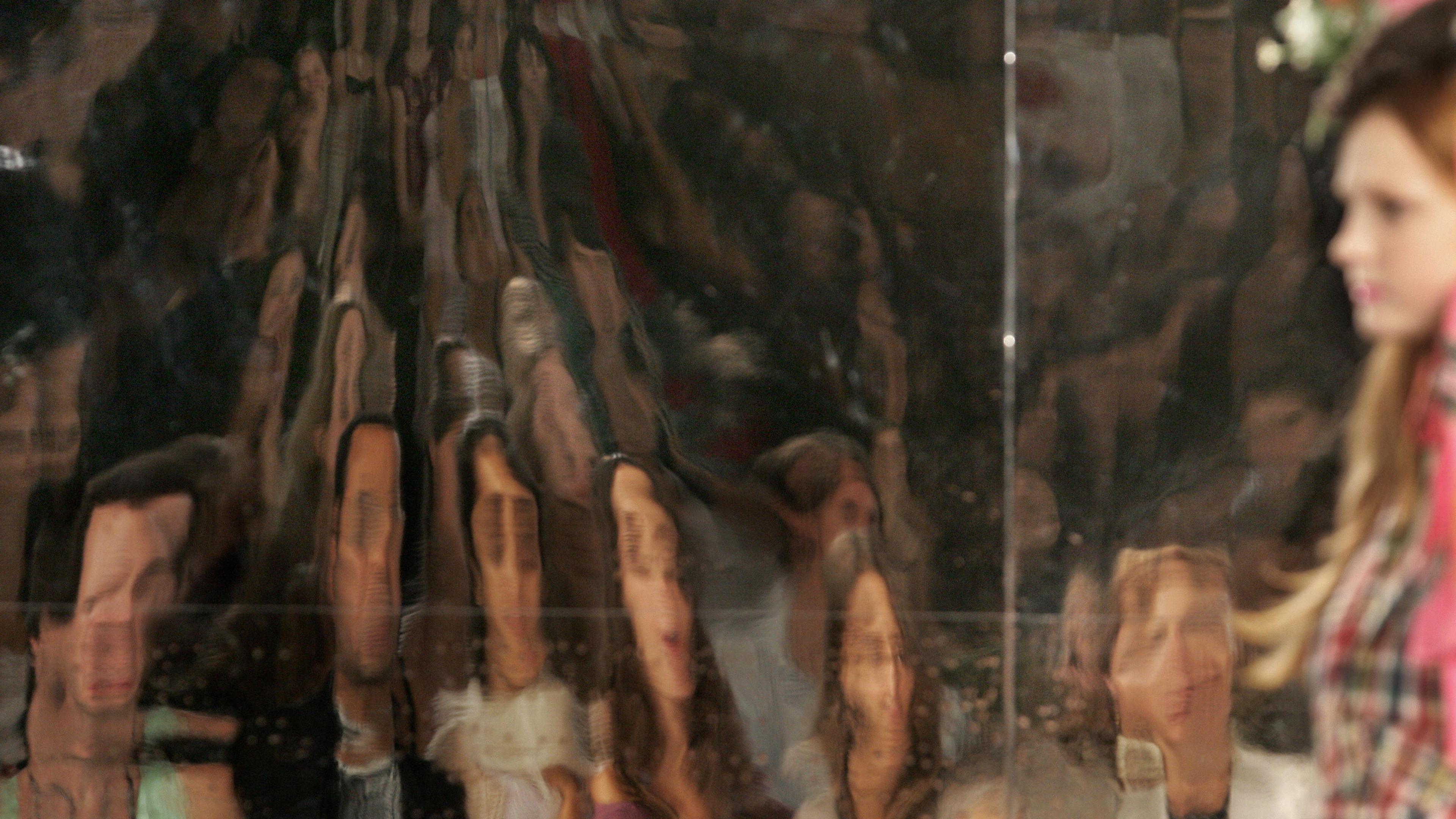 Distorted reflections of people on a textured surface next to a blurred person on the right, in a photo.