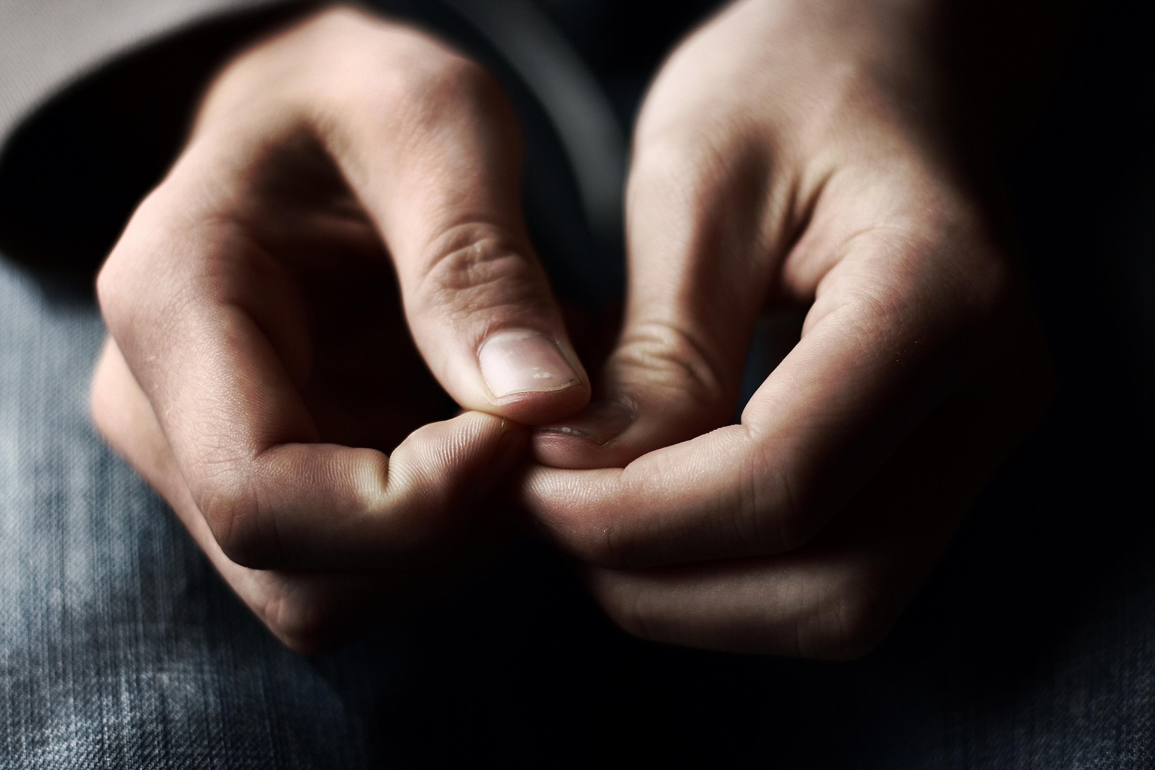 Photo of hands nervously fidgeting with fingers in focus, soft background of dark jeans visible.
