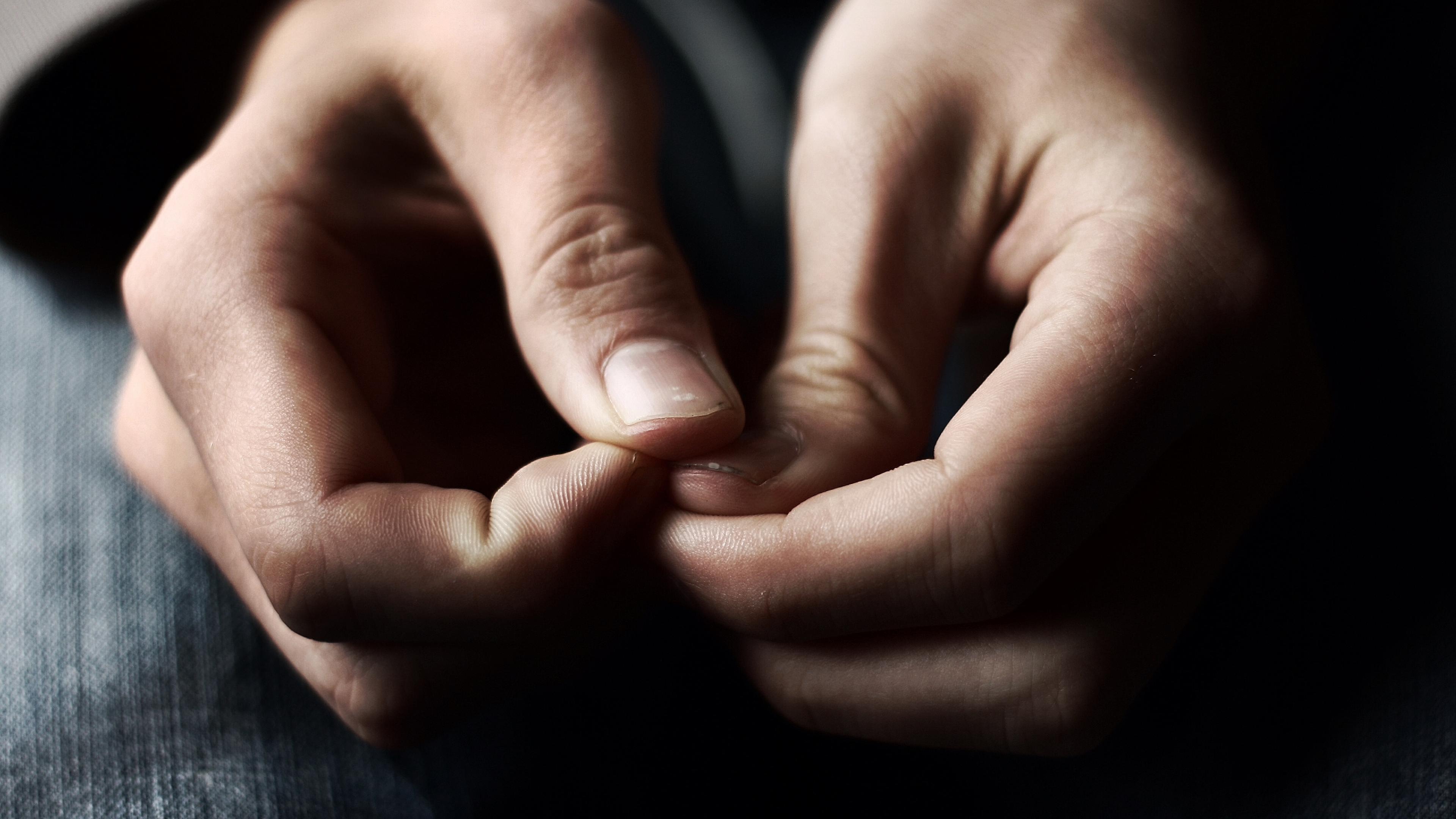 Photo of hands nervously fidgeting with fingers in focus, soft background of dark jeans visible.