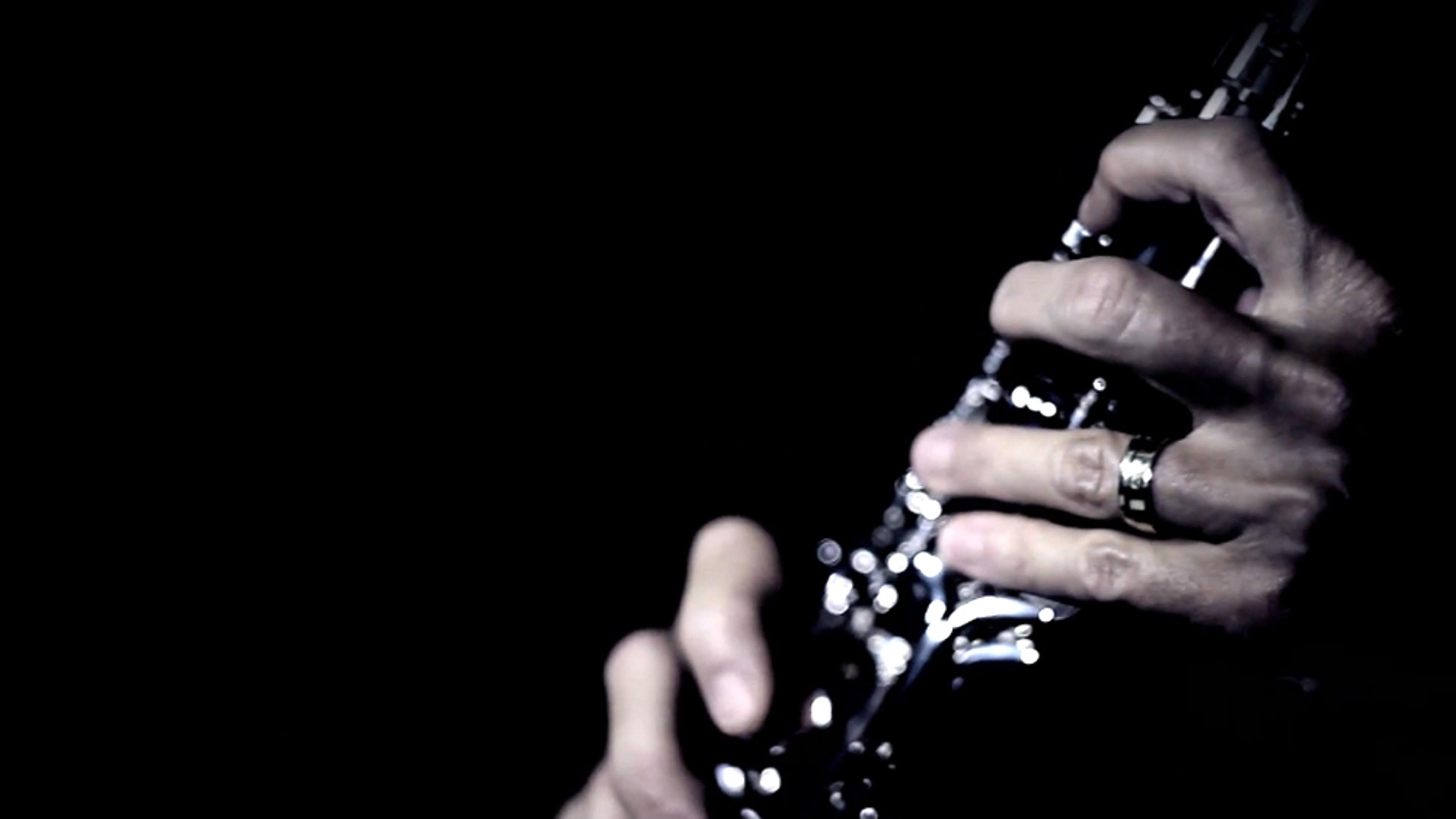 A person’s hands playing a clarinet against a dark background. The fingers are positioned on the clarinet keys.
