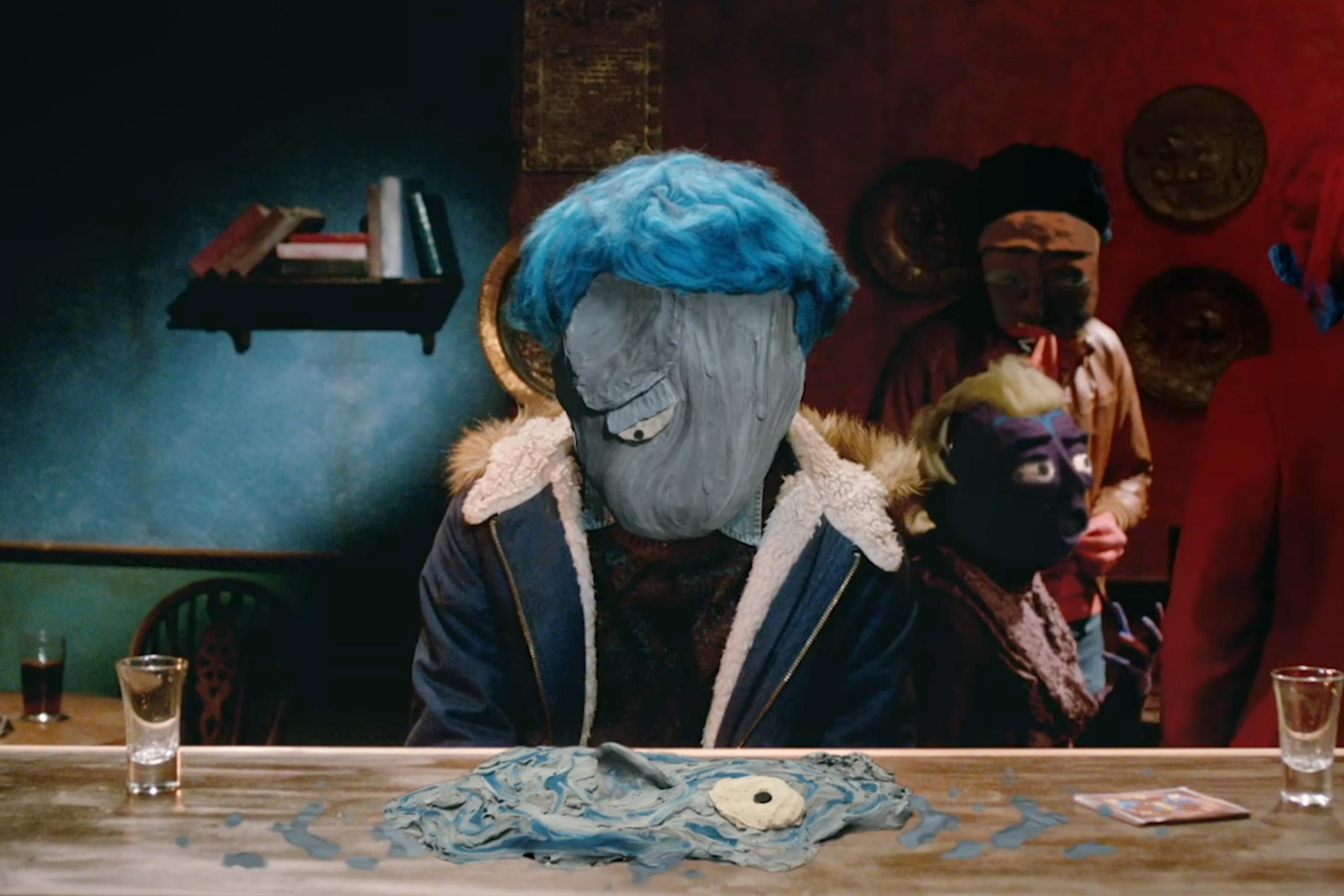 Surreal scene of a person with a clay mask and blue hair at a table with others in masks in the background, in a dimly lit room.