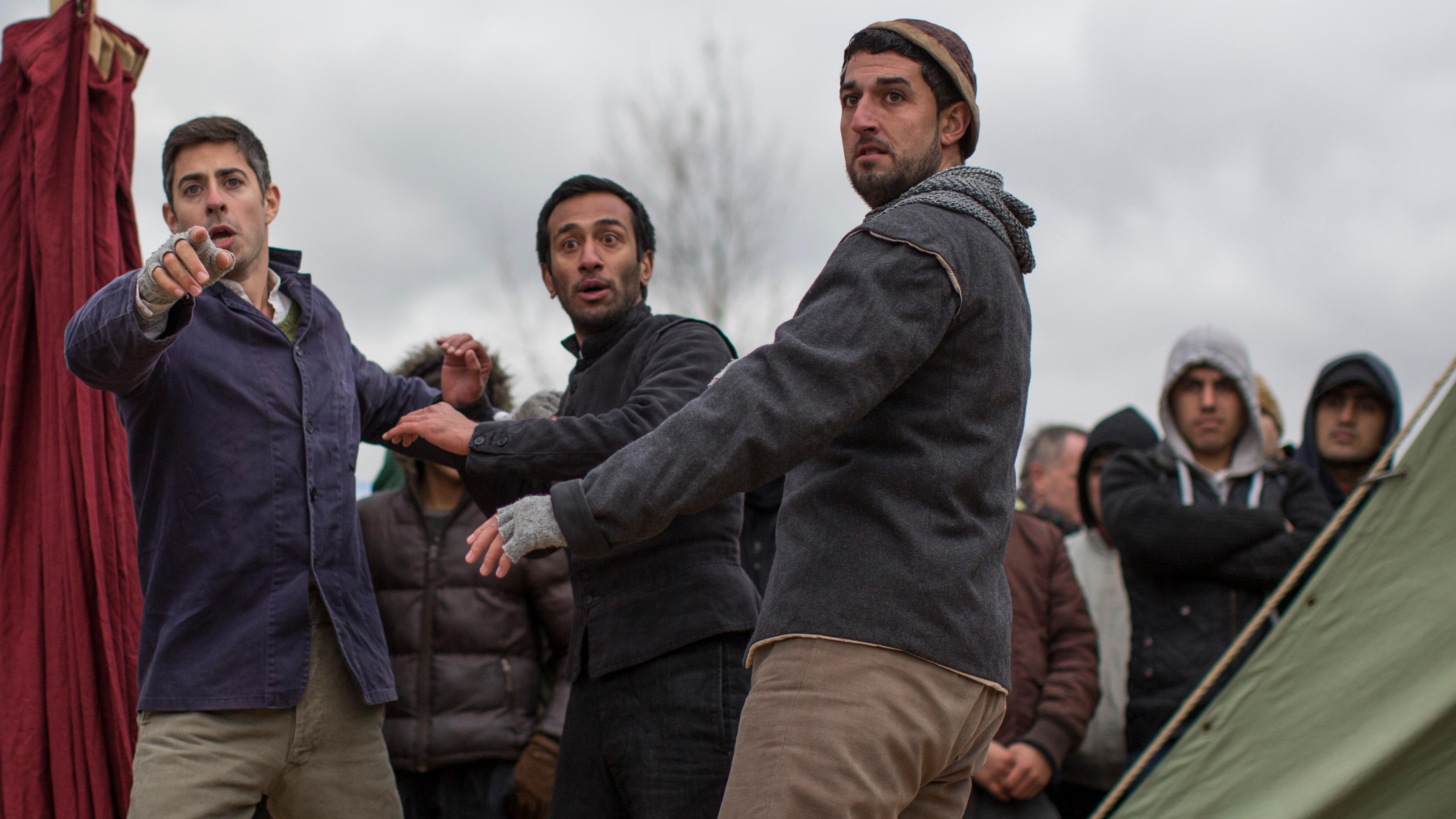 Photo of three men in jackets and beanies looking intently, with a group of people in the background on a cloudy day.
