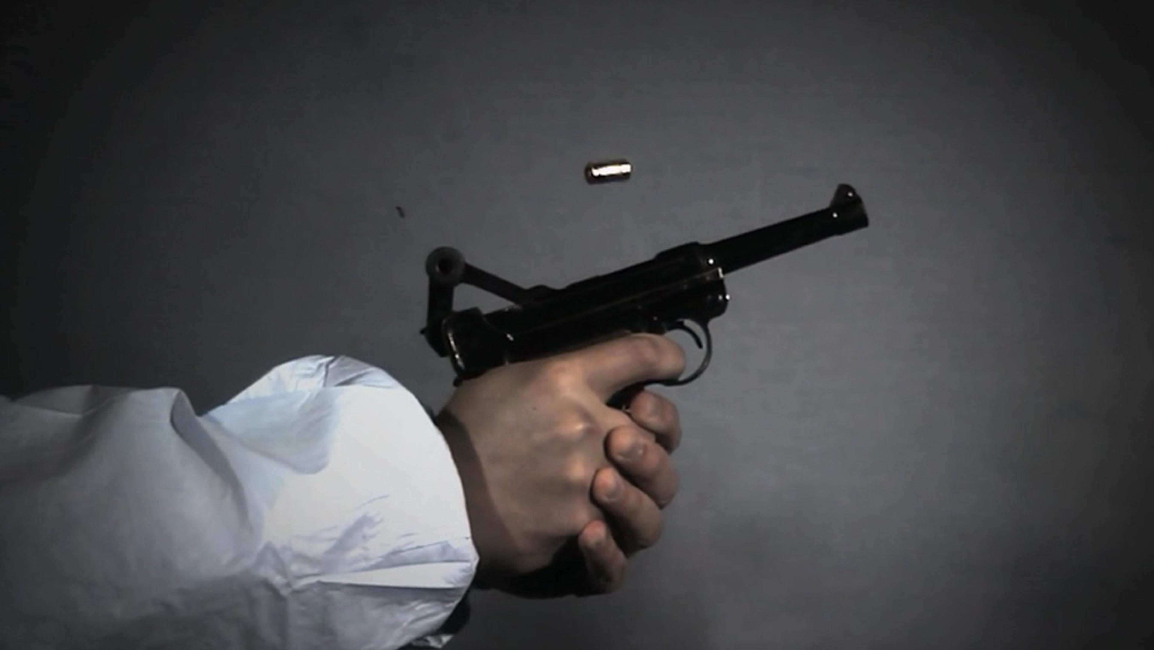 A photo of a hand in a white sleeve firing a black handgun with a bullet casing ejected mid-air against a dark background.