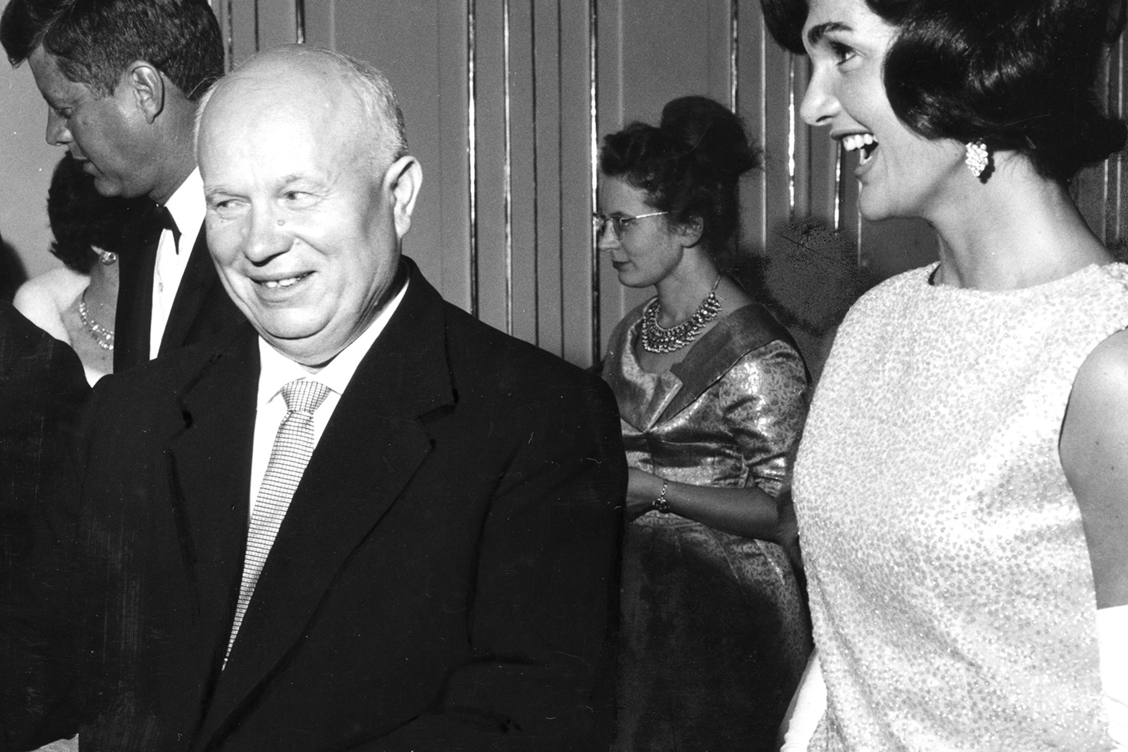 Black and white photo of a man smiling next to a woman laughing at a formal event. Other guests visible in the background.
