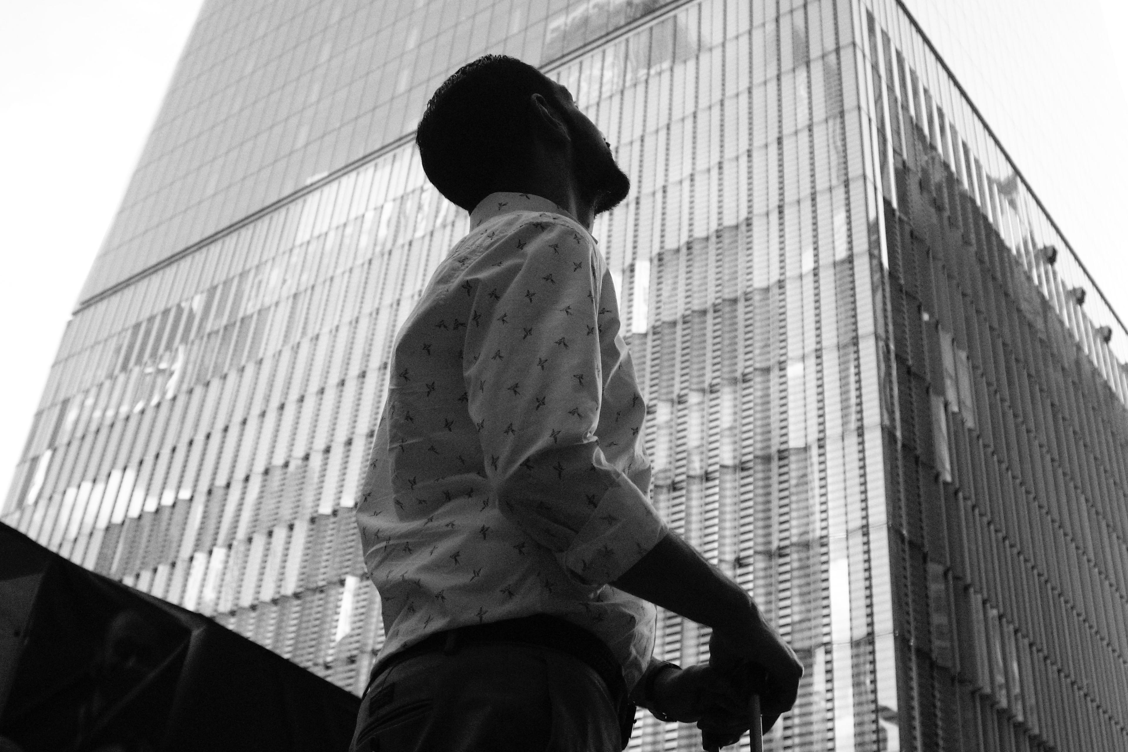 Black and white photo of a person looking up at a tall glass skyscraper with a suitcase in hand.