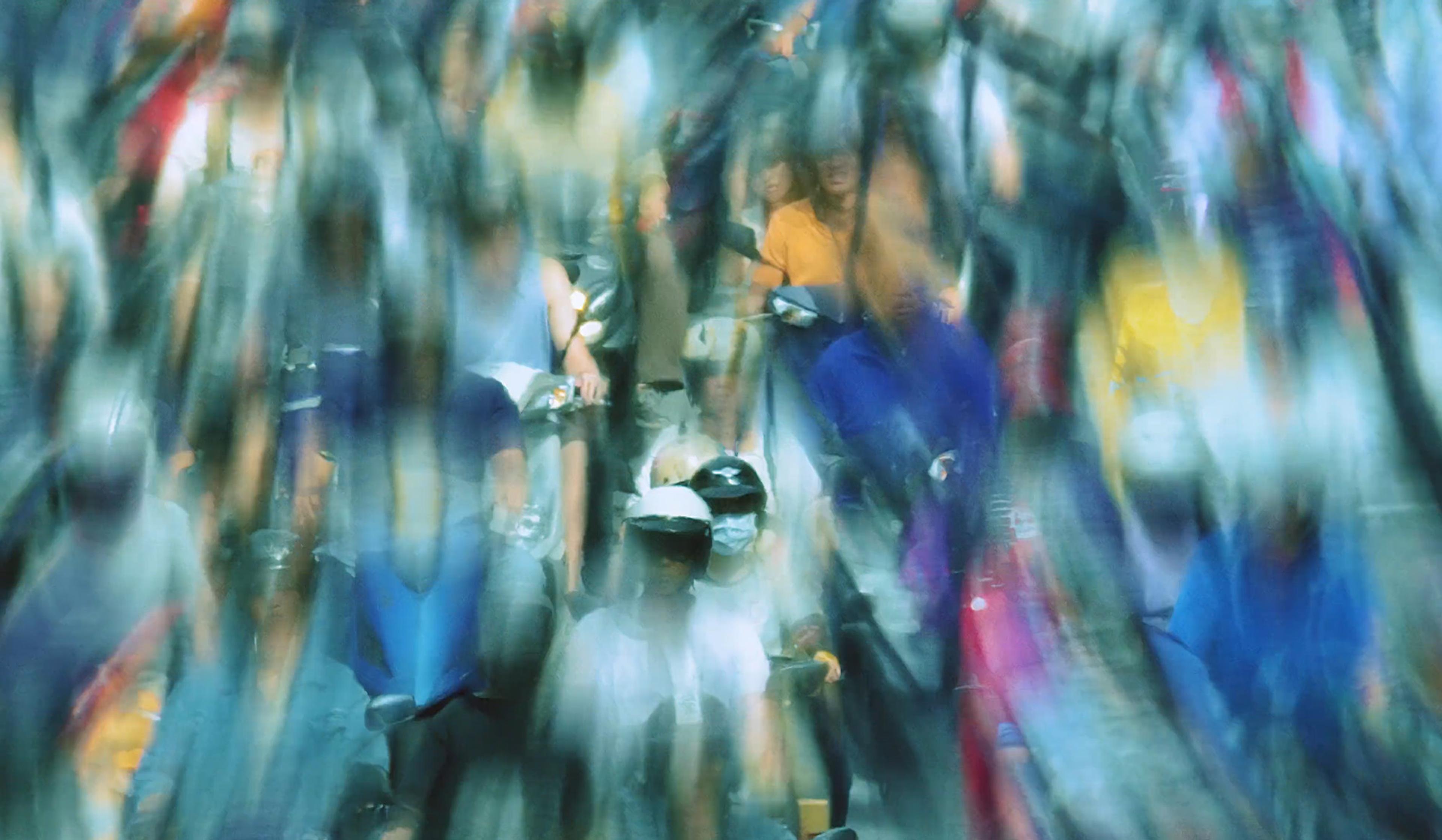 Blurred photo of a large crowd of people on motorbikes and scooters, creating a sense of motion and activity.