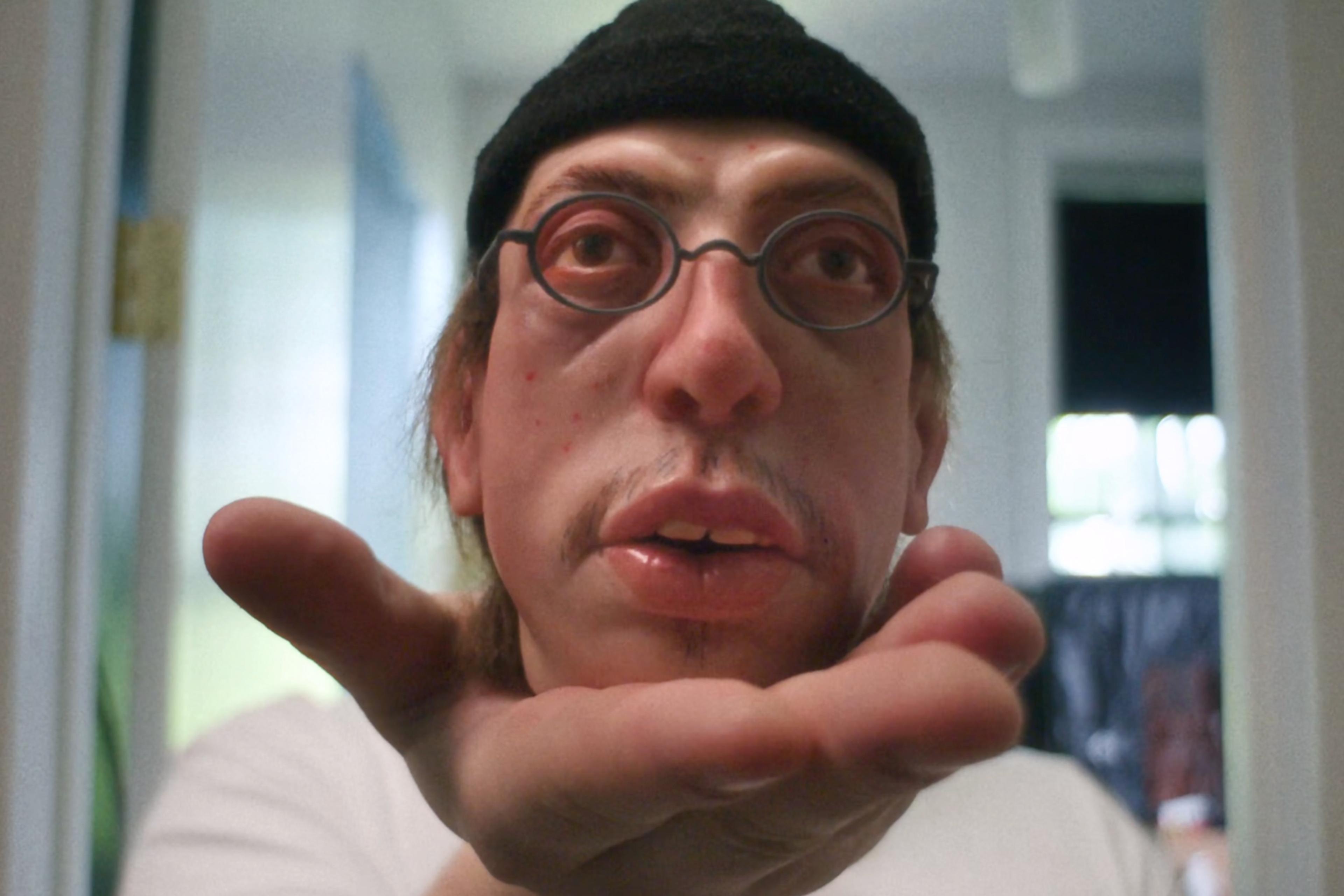 Surreal photo of a person wearing glasses and a hat with their face distorted, leaning towards a camera in a hallway.