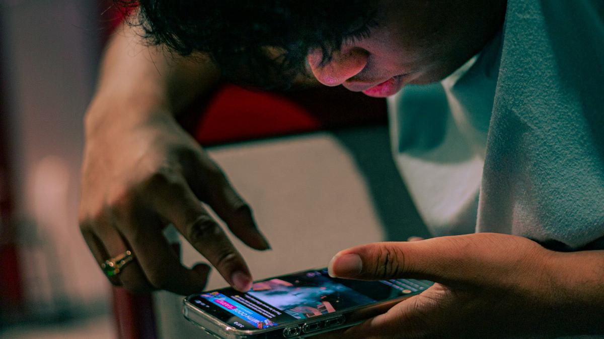 A person using a smartphone, with focus on their finger scrolling the screen. Face partially visible.