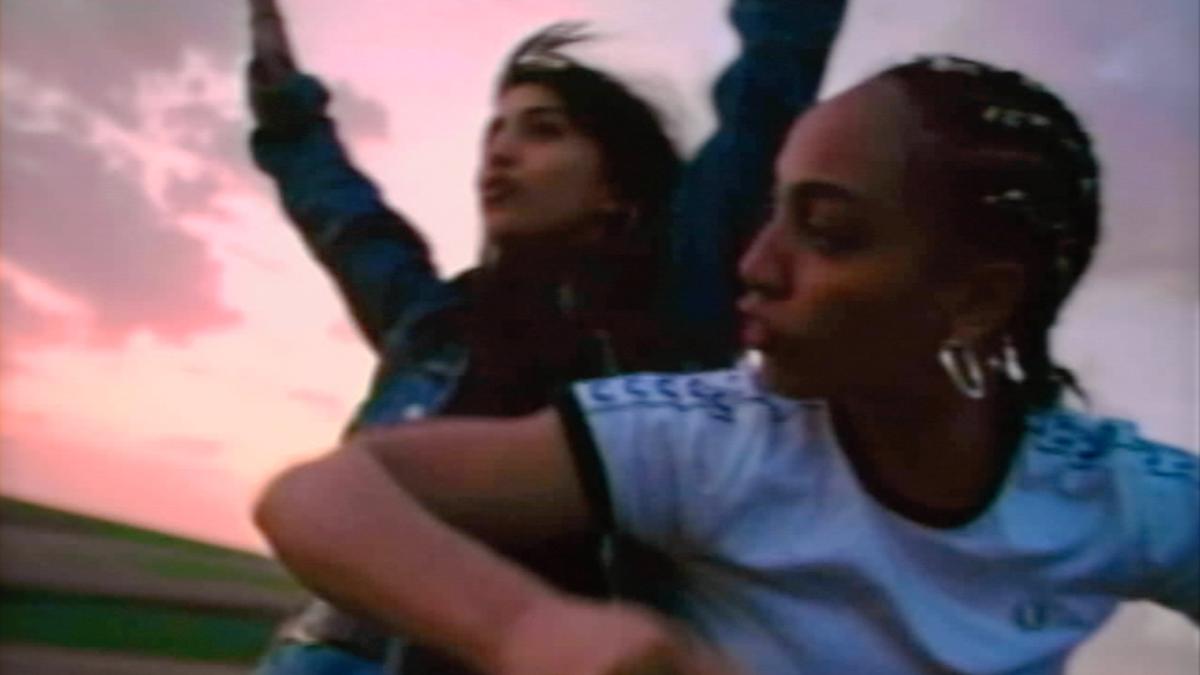 Two people enjoying a scenic sunset with one raising their arms and the other looking sideways, in an outdoor setting.