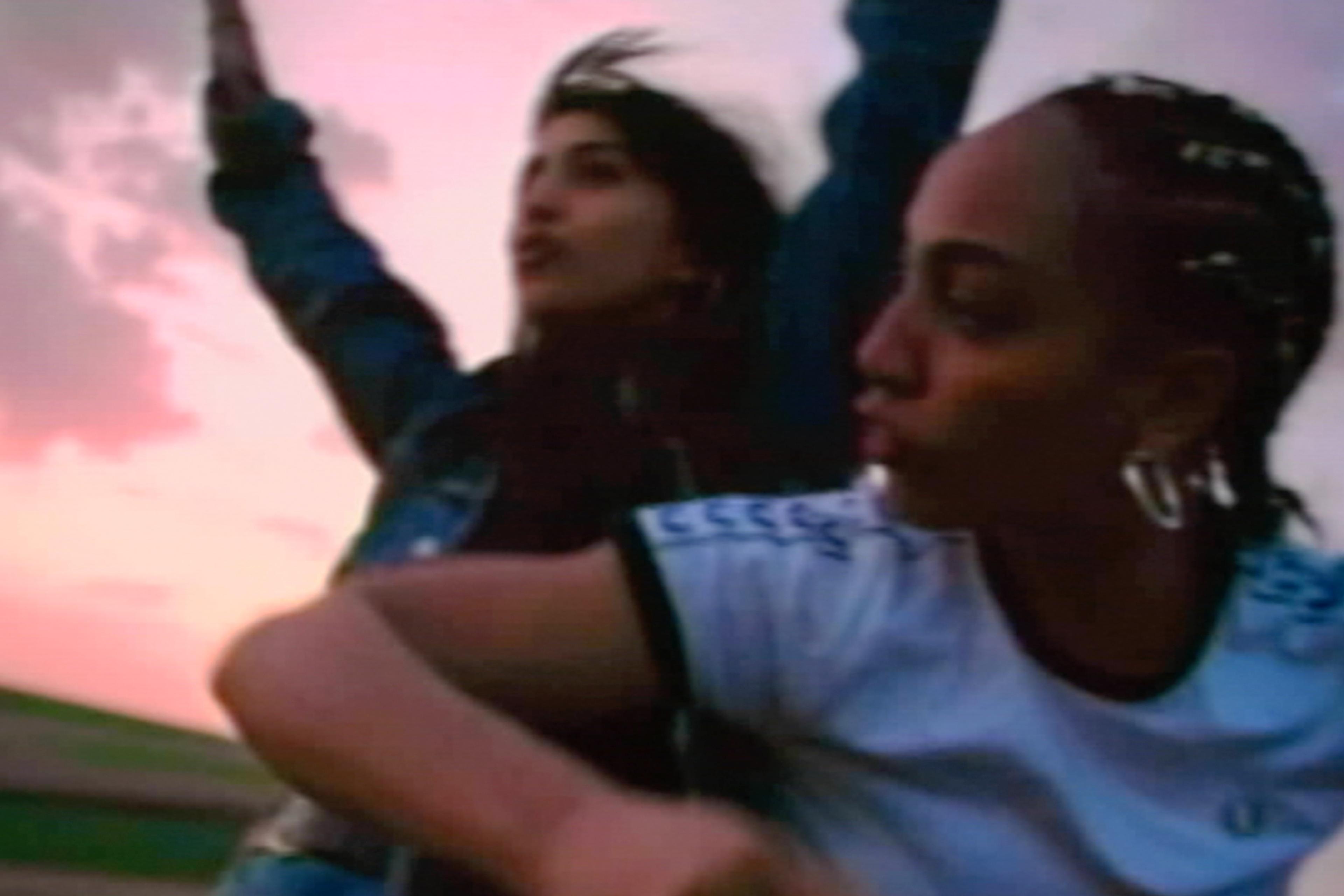 Two people enjoying a scenic sunset with one raising their arms and the other looking sideways, in an outdoor setting.
