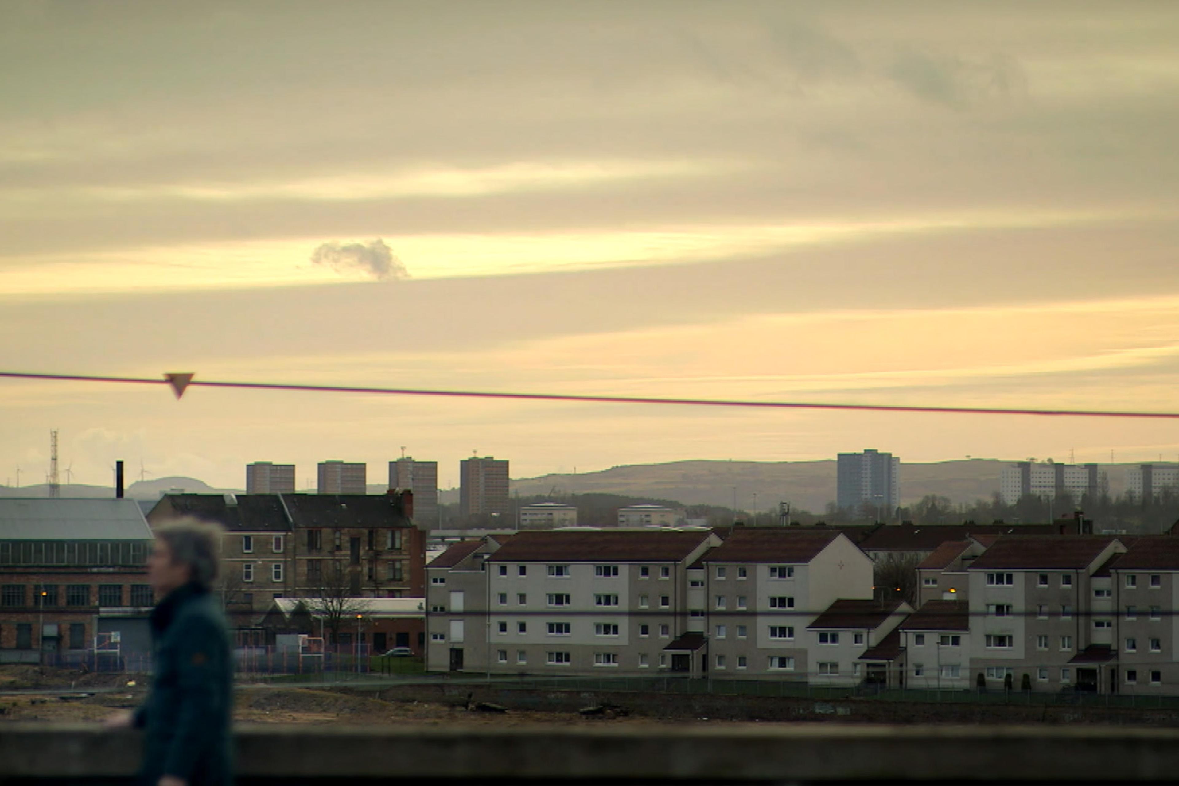 Image of an urban housing area at dusk with a distant view of apartment buildings and a blurred figure in the foreground.