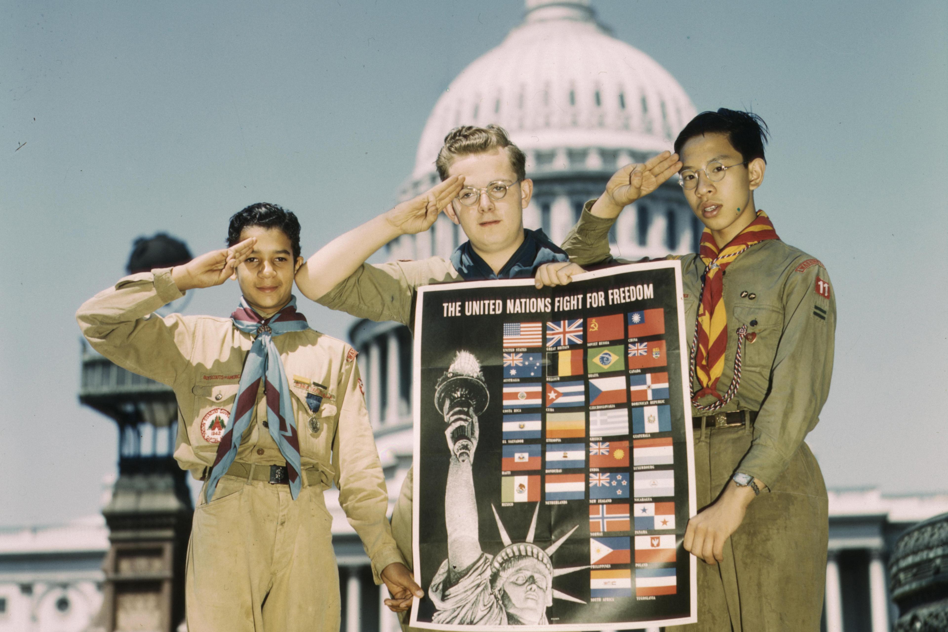 Photo of three scouts saluting, holding a poster of flags and the Statue of Liberty, in front of the US Capitol building.