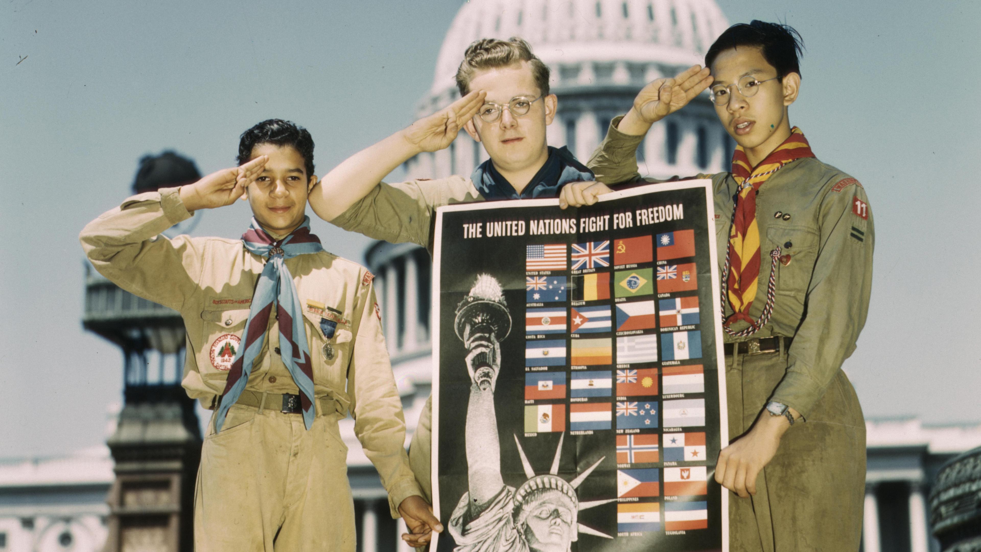 Photo of three scouts saluting, holding a poster of flags and the Statue of Liberty, in front of the US Capitol building.