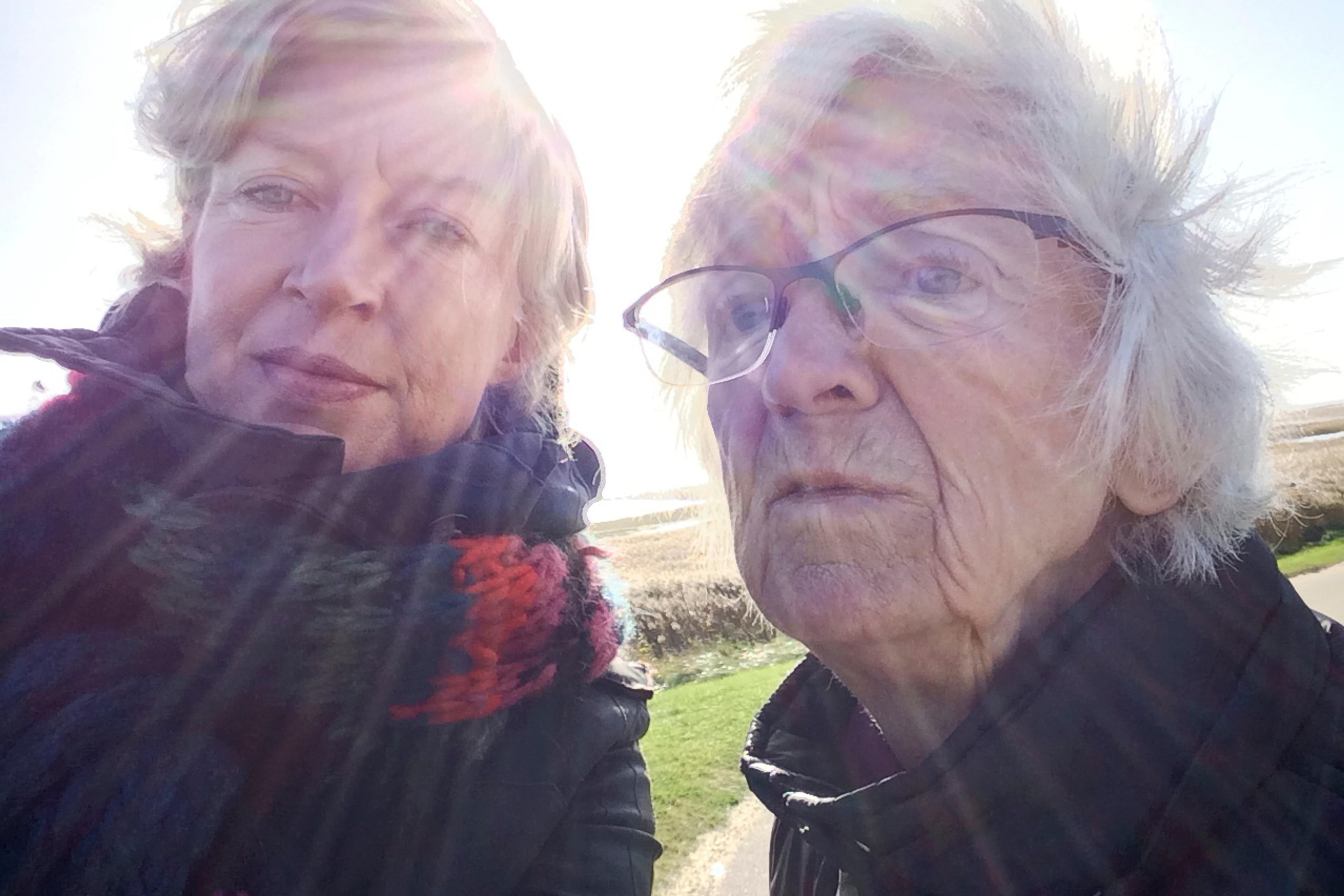 Photo of two people outdoors in winter clothing with sun rays surrounding them. One person wears glasses. Bright sky in background.