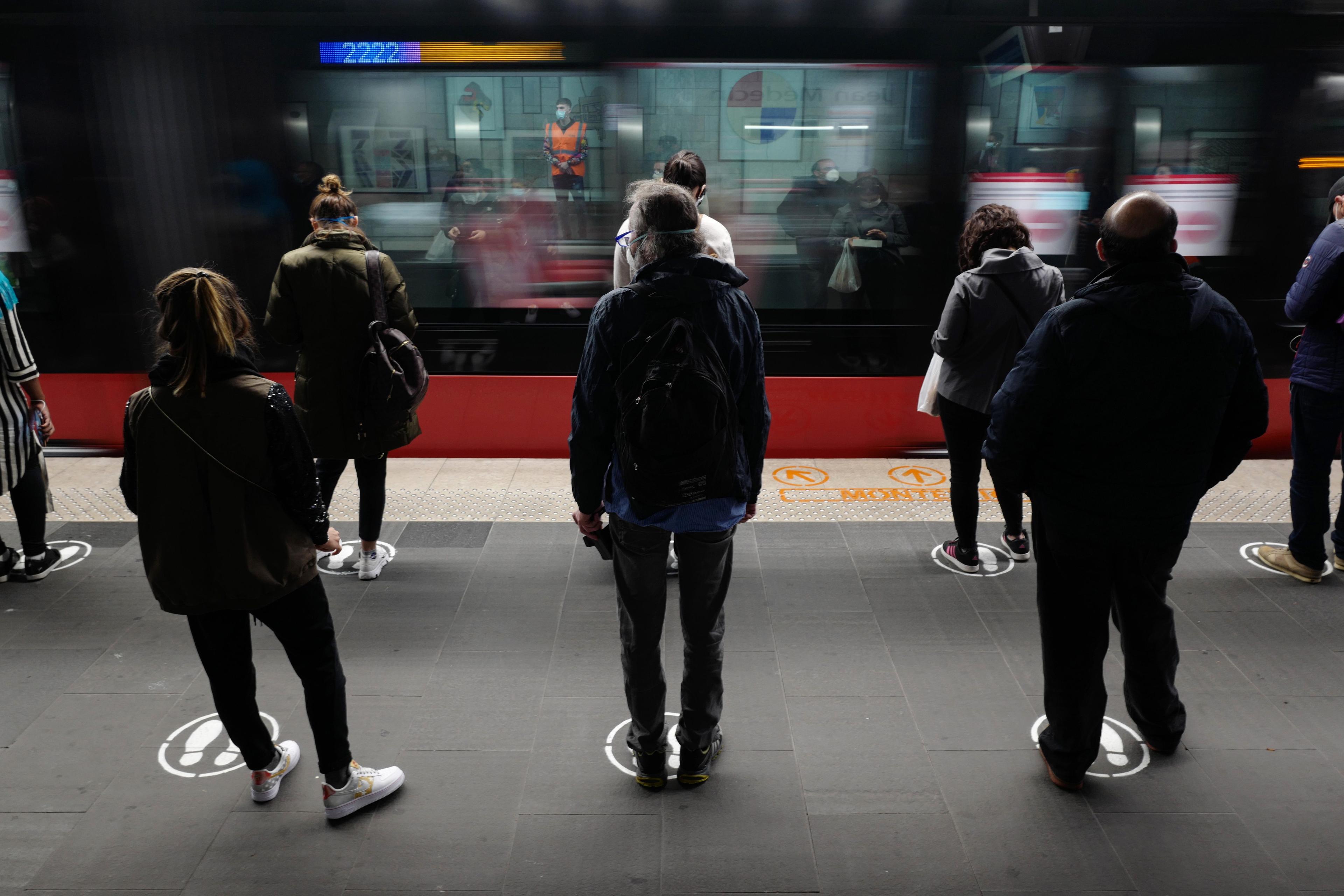 Photo of people waiting on a train platform standing on marked spots as a train speeds past in the background.