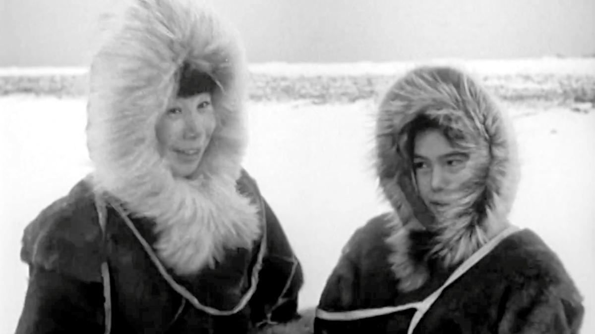 Black and white film still of two people in fur-lined parkas in a snowy landscape.