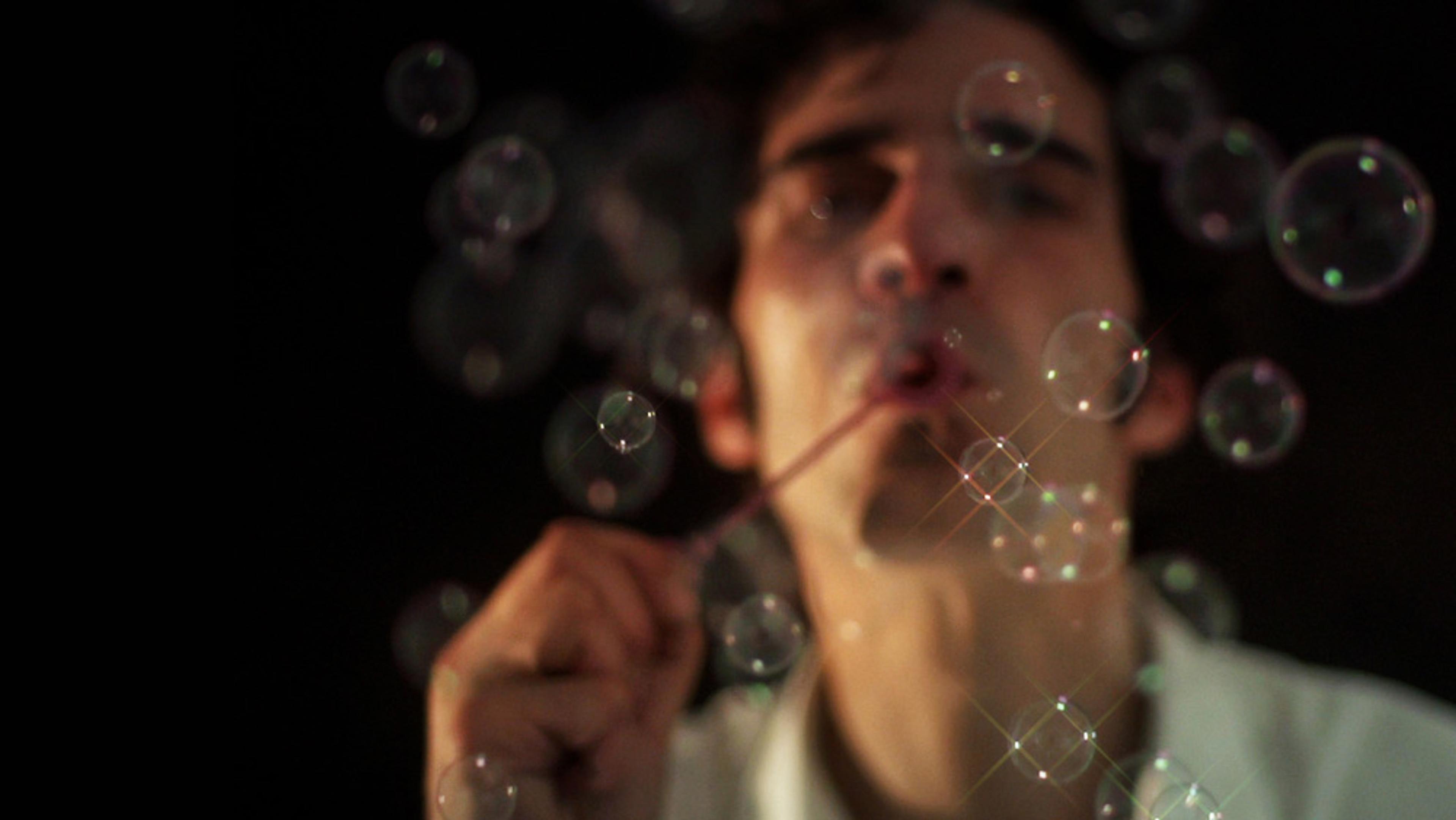 A man blowing soap bubbles with a dark background; the image is out of focus, highlighting the bubbles.