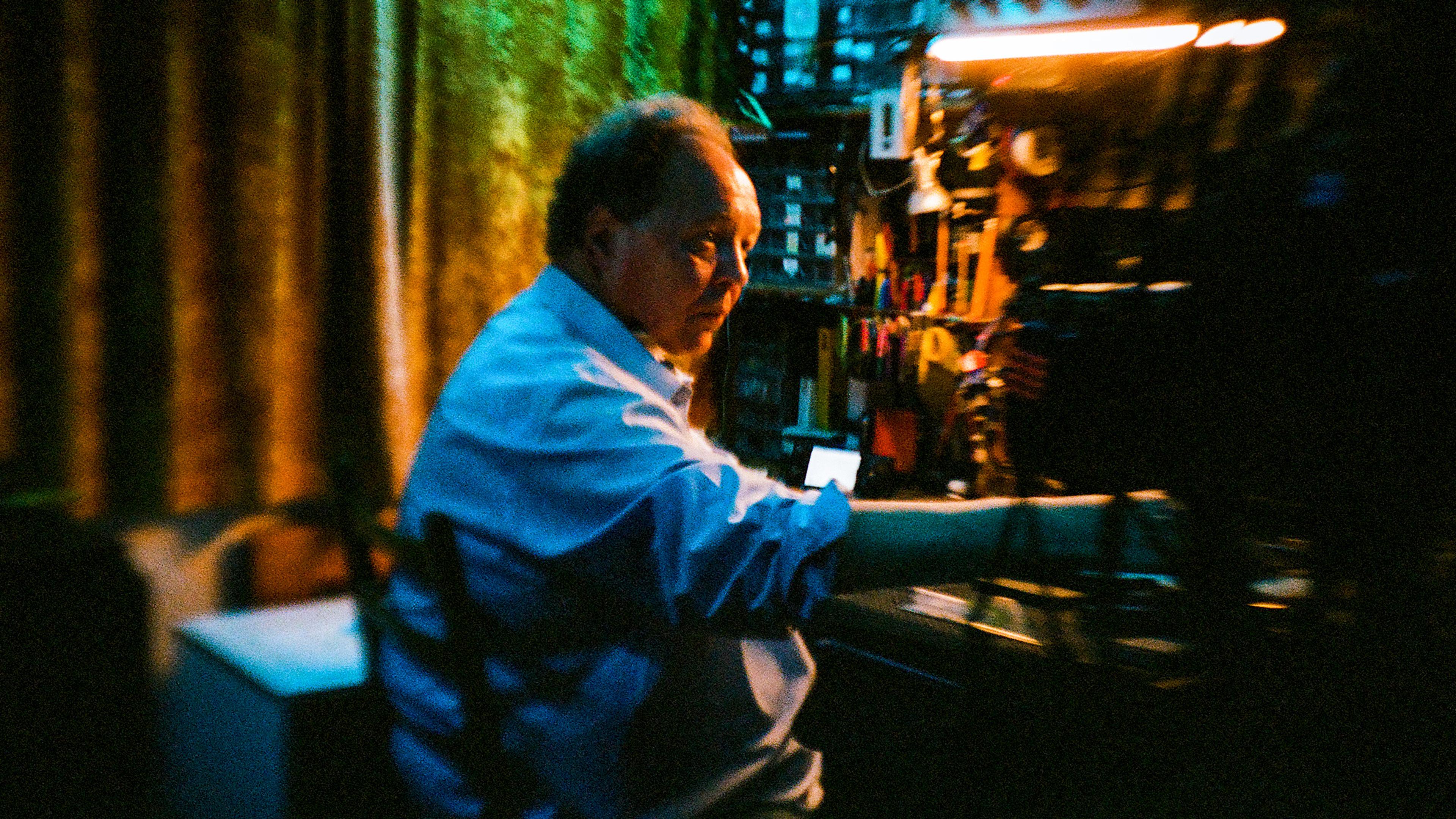 Photo of a man in a workshop illuminated by warm light, surrounded by tools with a focused expression.