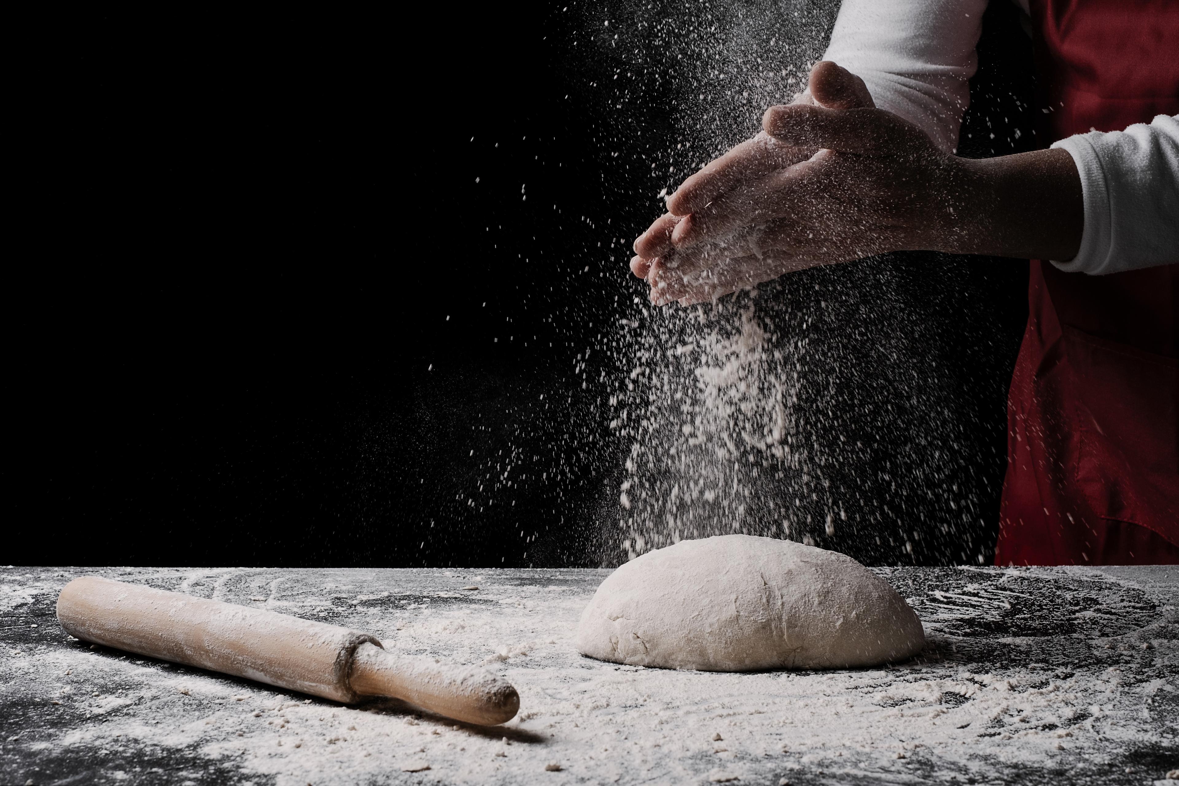 Photo of a person dusting flour on a dough ball with a rolling pin nearby on a flour-covered surface.