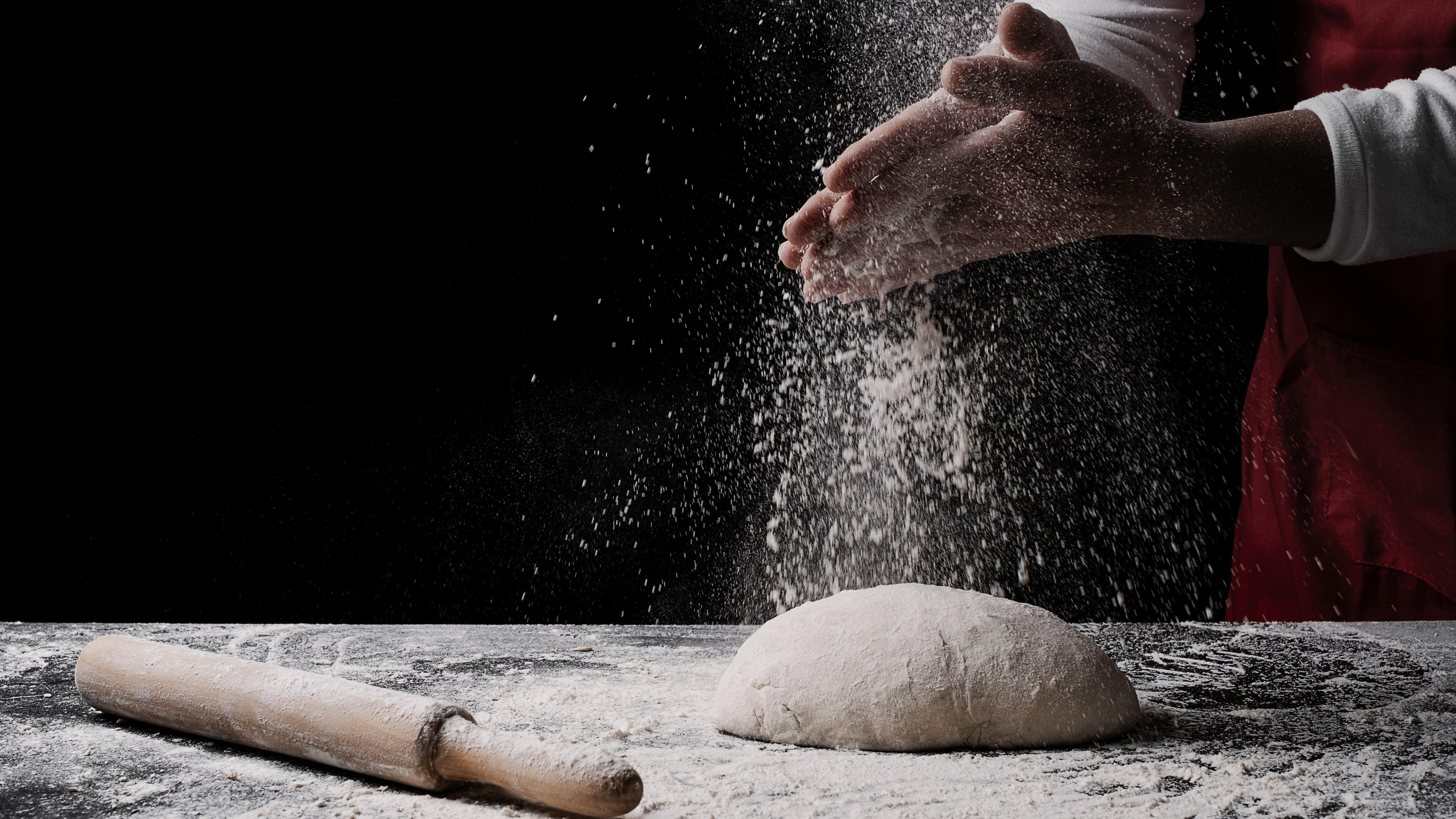Photo of a person dusting flour on a dough ball with a rolling pin nearby on a flour-covered surface.