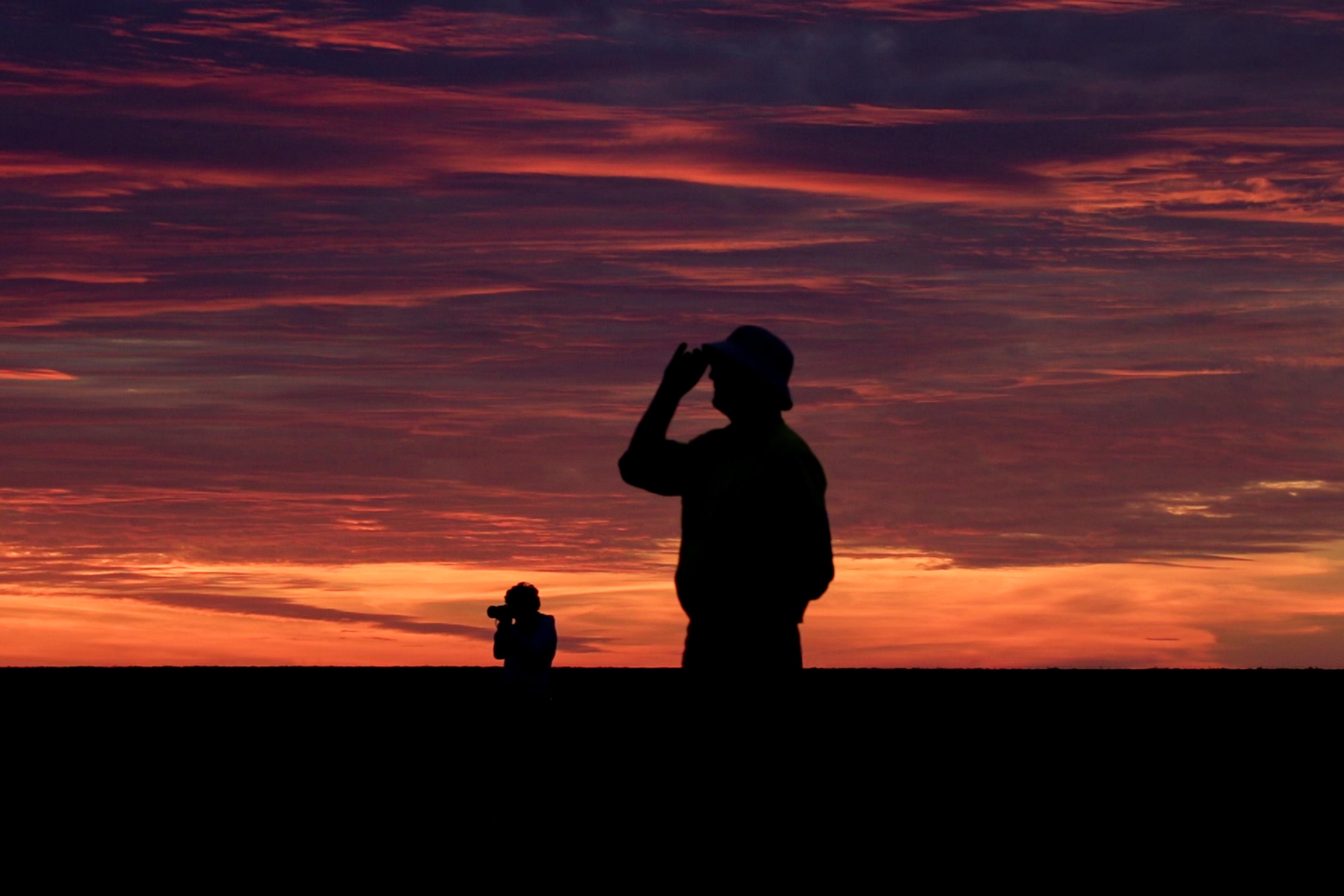 Two silhouetted people stand against a dramatic orange and purple sunset sky.