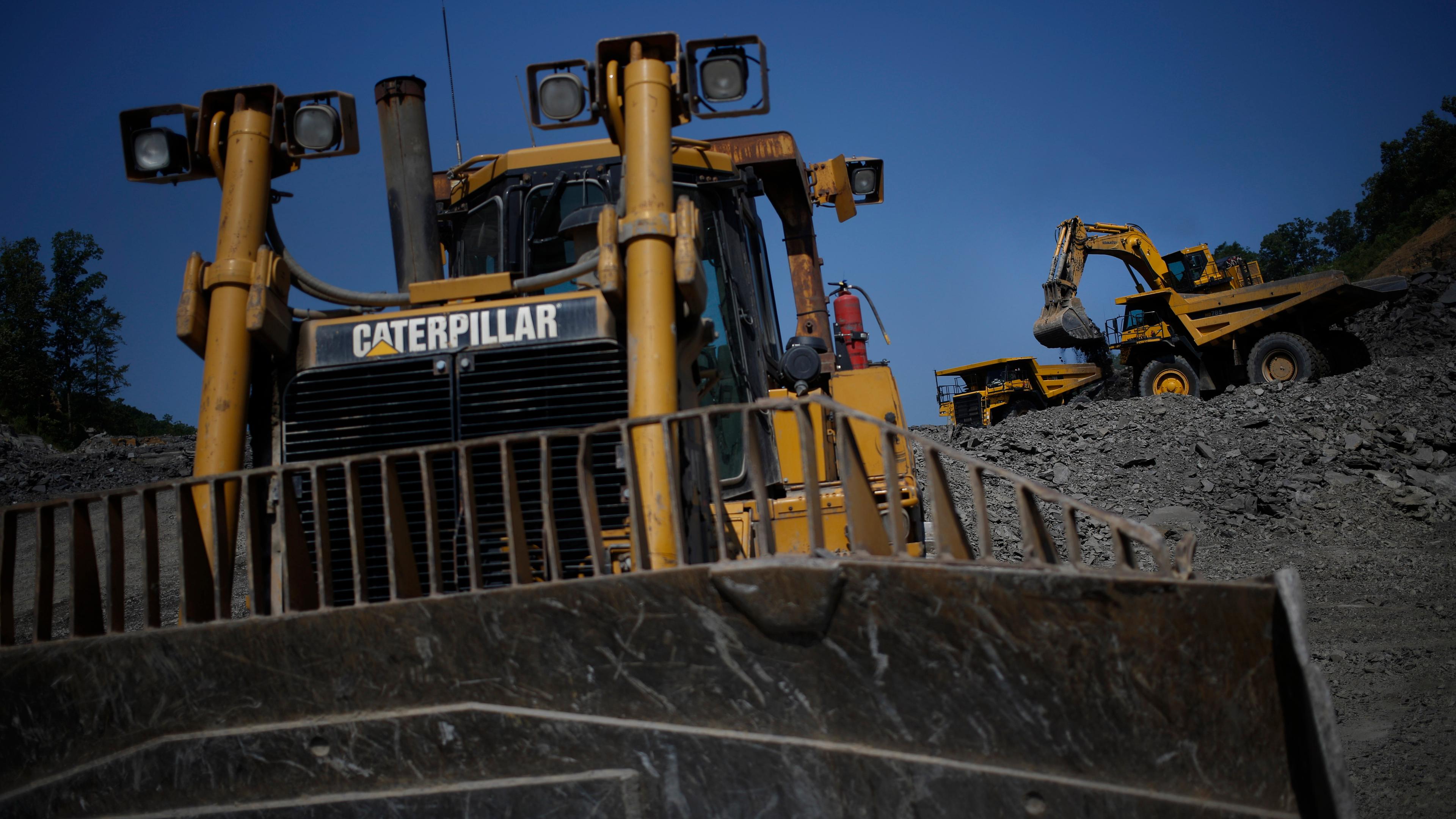 A bulldozer and excavator at a quarry with a clear blue sky in the background.