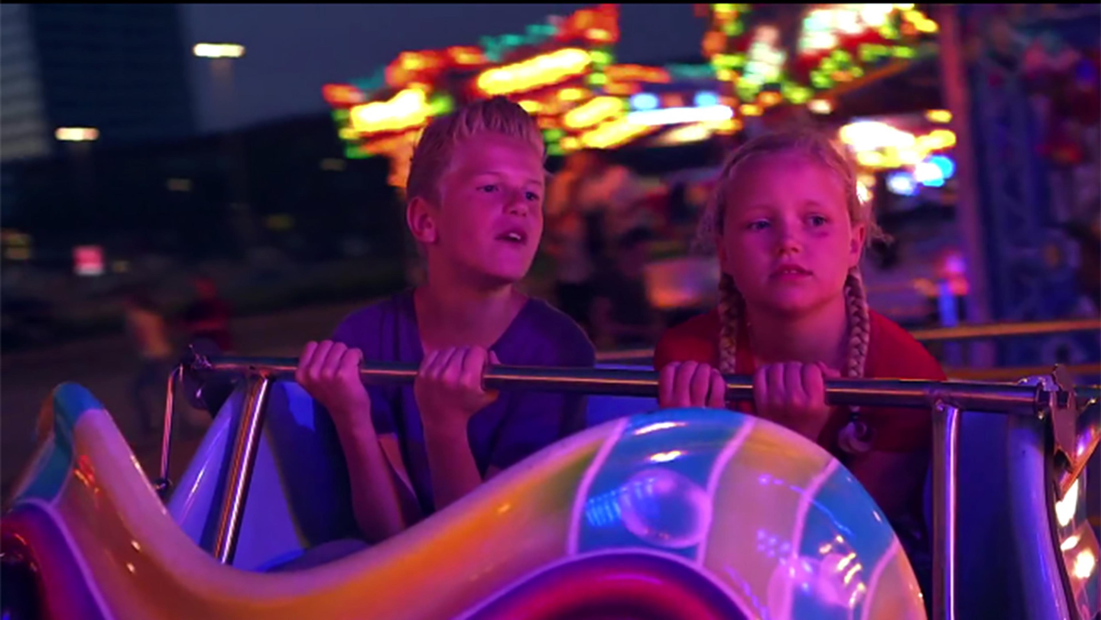 Two children on a carnival ride at night holding onto the safety bar with blurred colourful lights in the background.