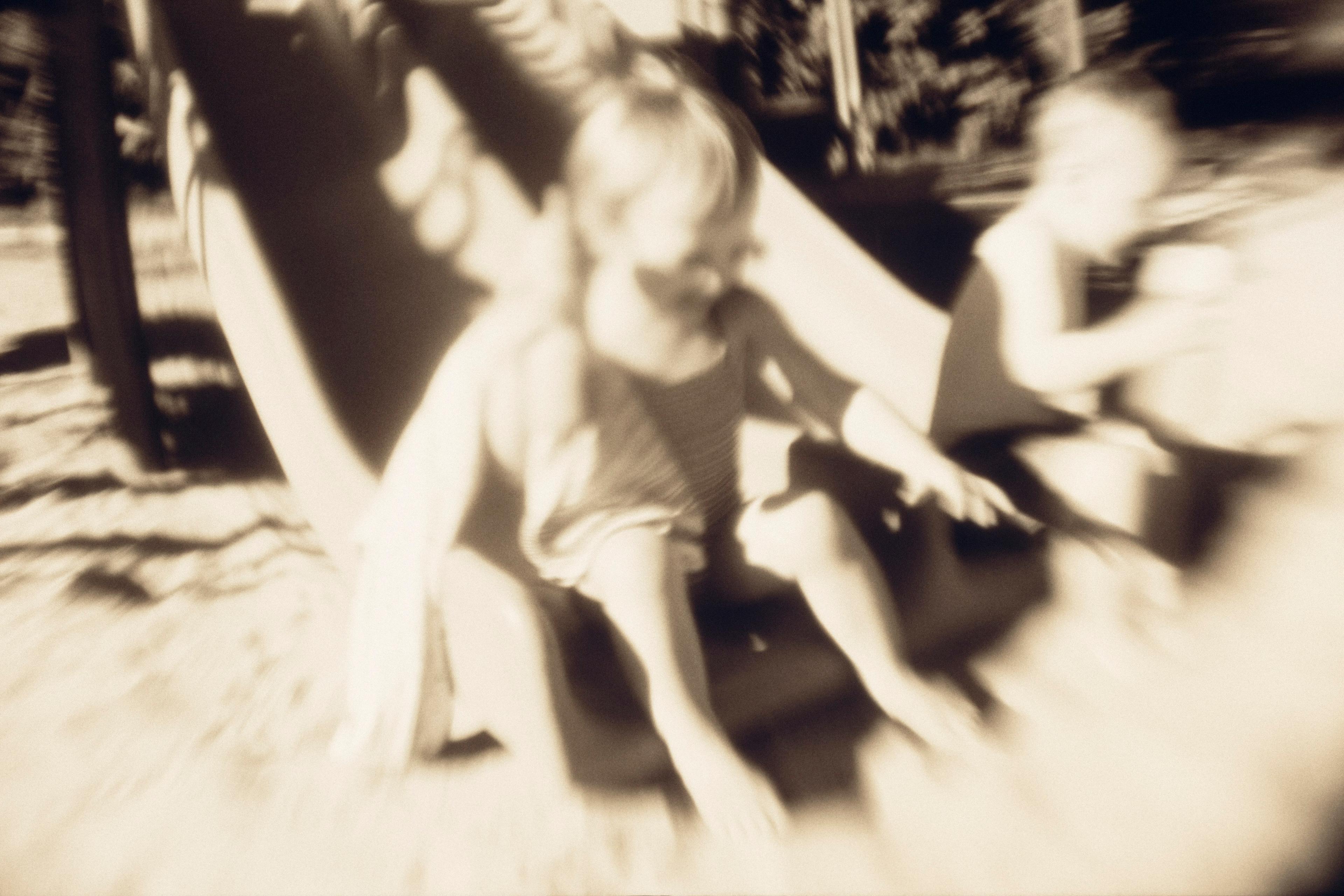 Blurry sepia photo of two children sliding down a playground slide in sunlight.
