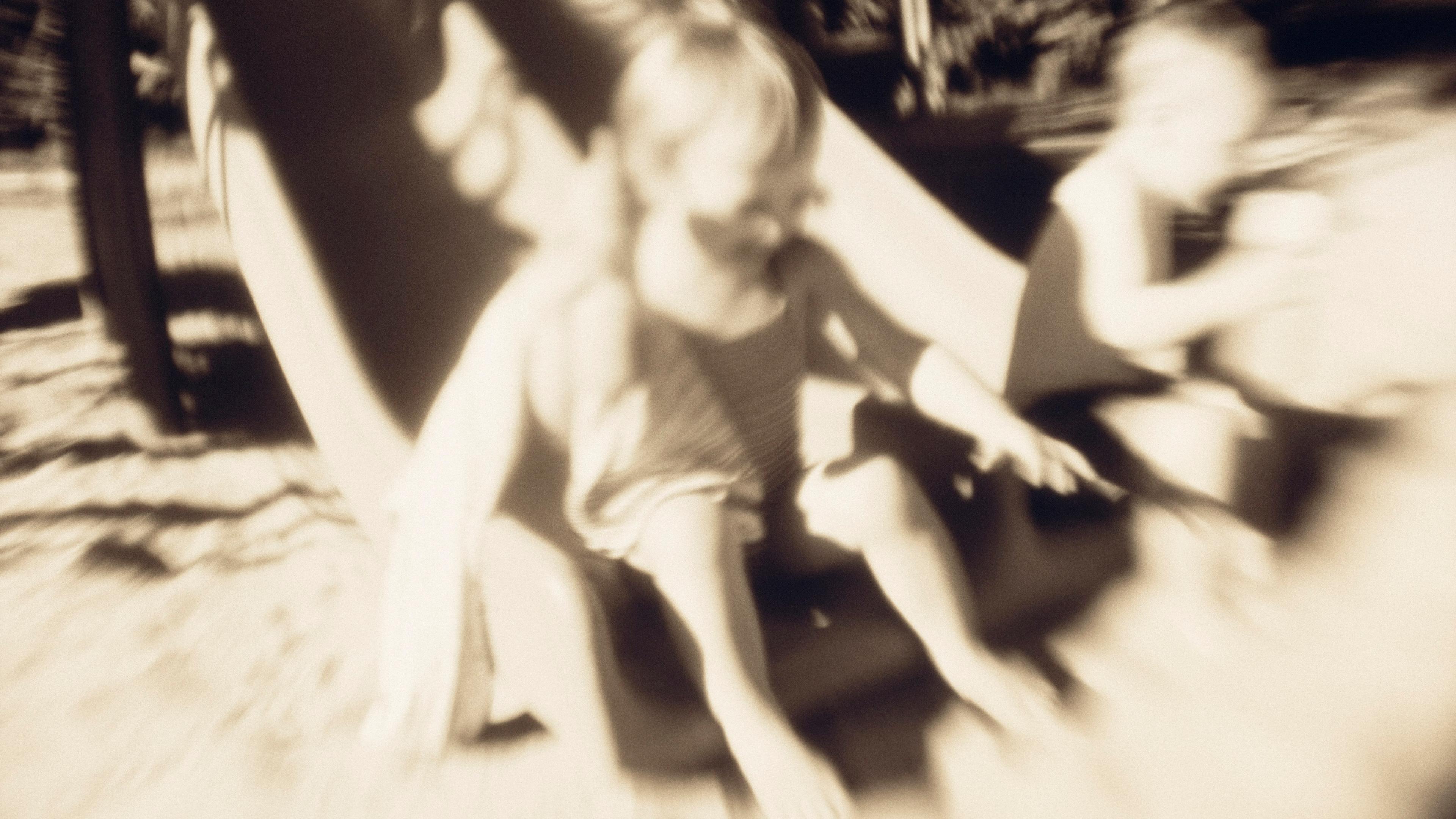Blurry sepia photo of two children sliding down a playground slide in sunlight.