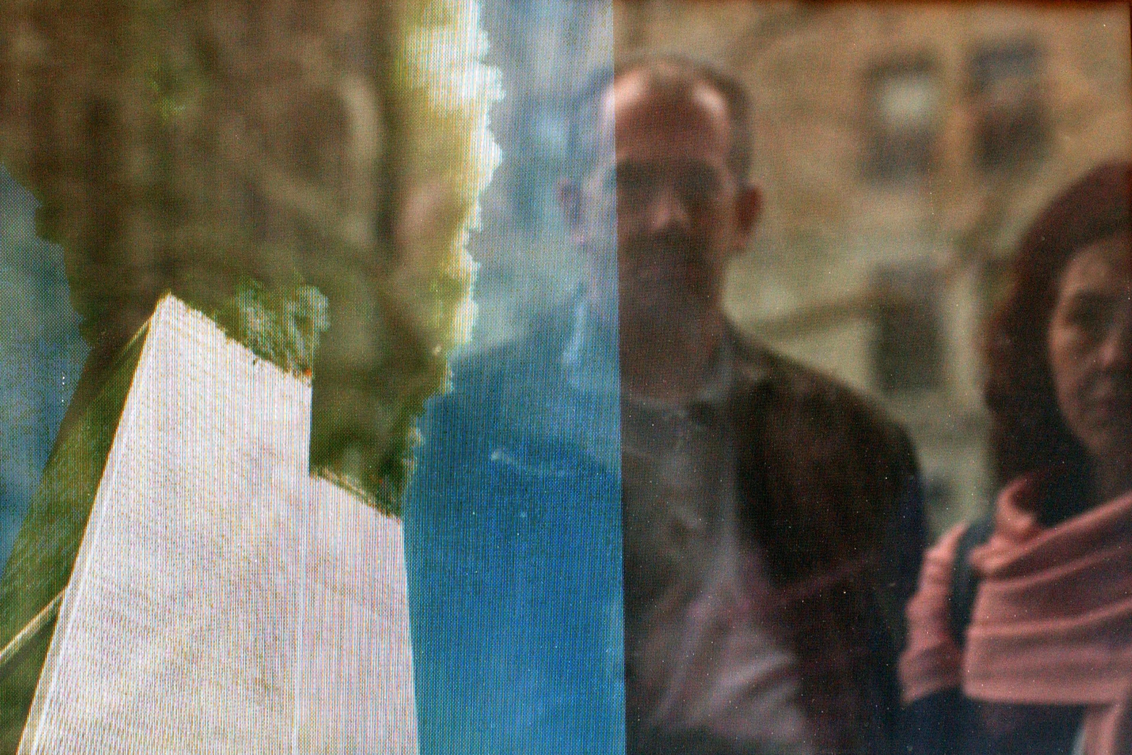 Photo of a burning tower with smoke, reflects a man and woman standing nearby in an urban setting.