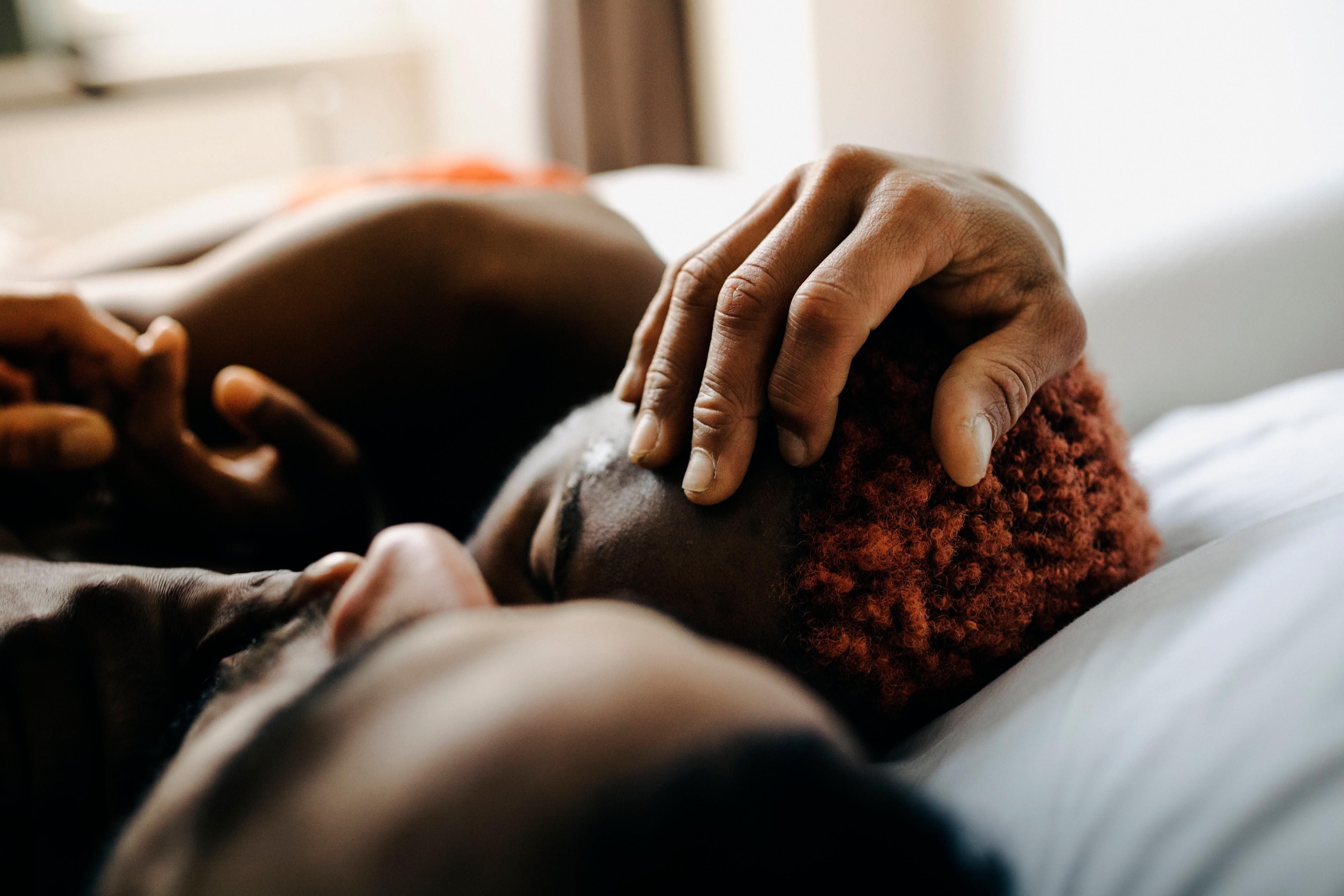 Photo of a close-up of an intimate moment between two people lying close, with one hand gently touching the other’s hair.