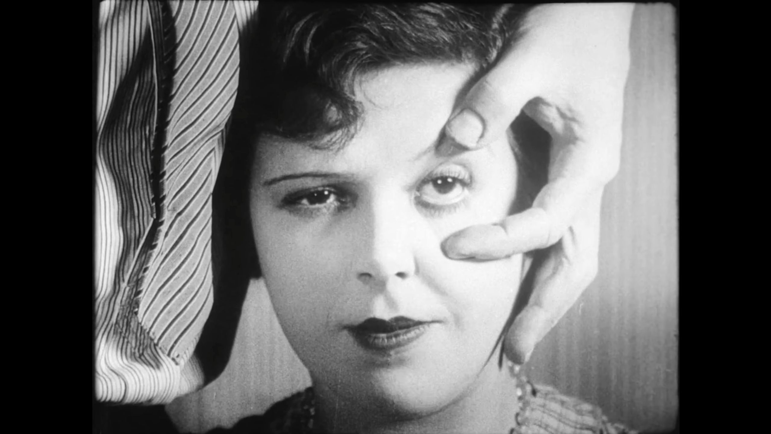 Black and white film still of a woman with a hand holding her eye open, showing surreal imagery.
