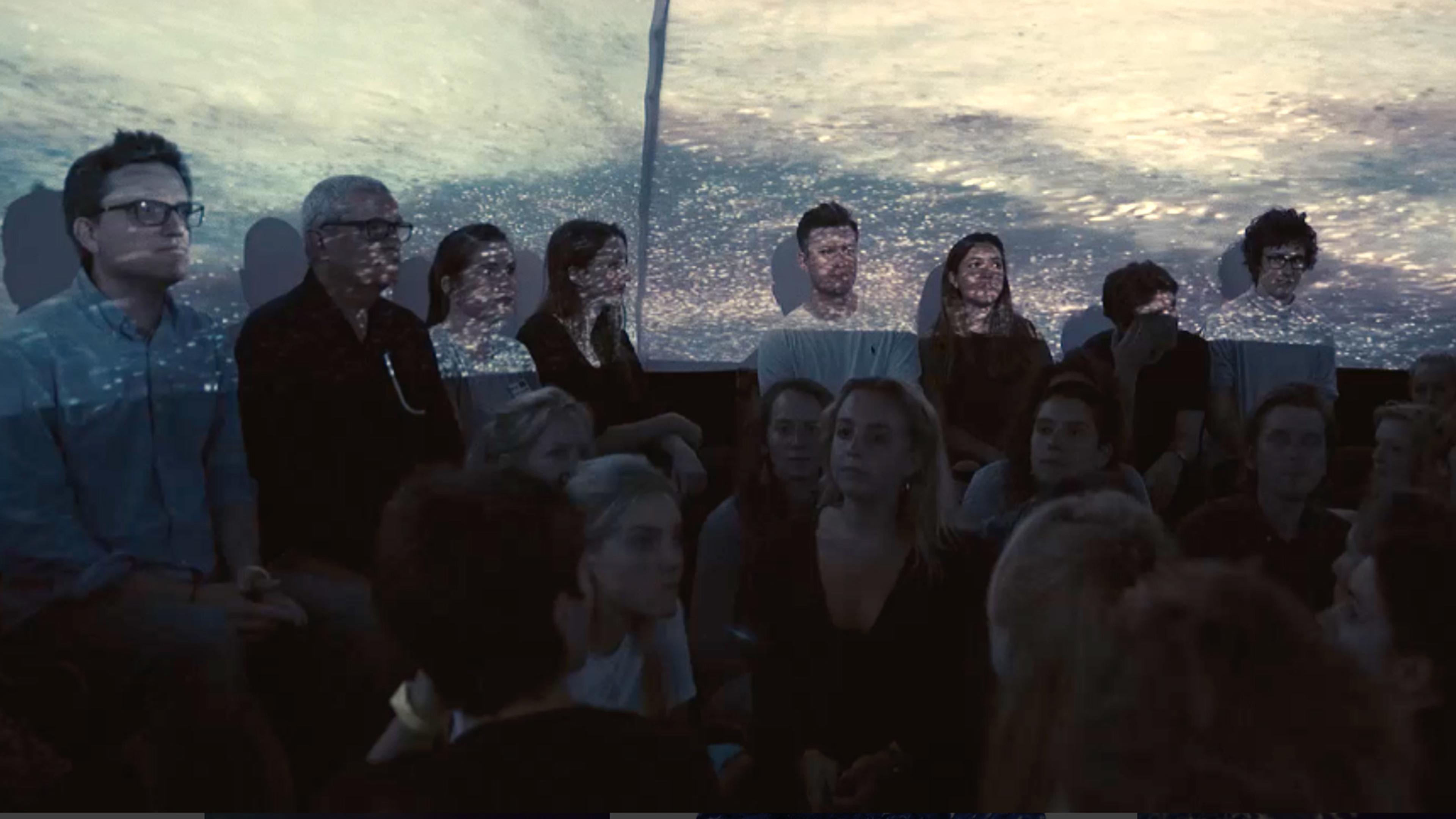 Audience with a seascape projected onto them, creating an artistic overlay of water and light.
