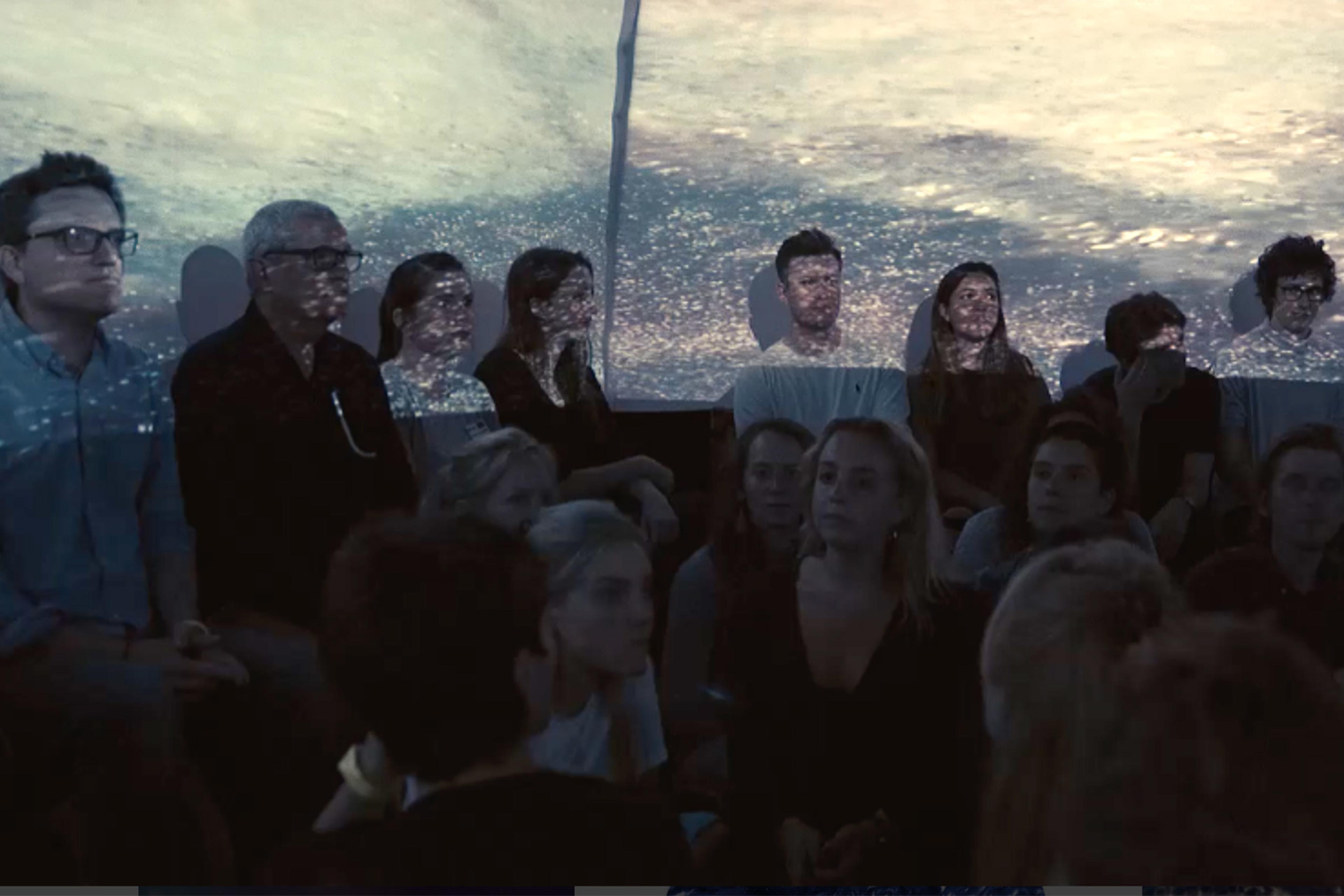 Audience with a seascape projected onto them, creating an artistic overlay of water and light.