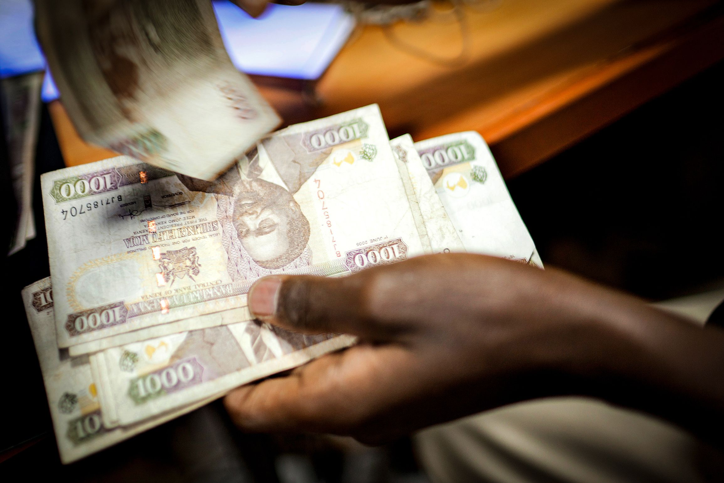 A person handling several 1000 Kenyan shilling banknotes at a desk, with motion blur on one note being moved.