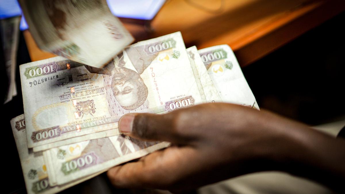 A person handling several 1000 Kenyan shilling banknotes at a desk, with motion blur on one note being moved.