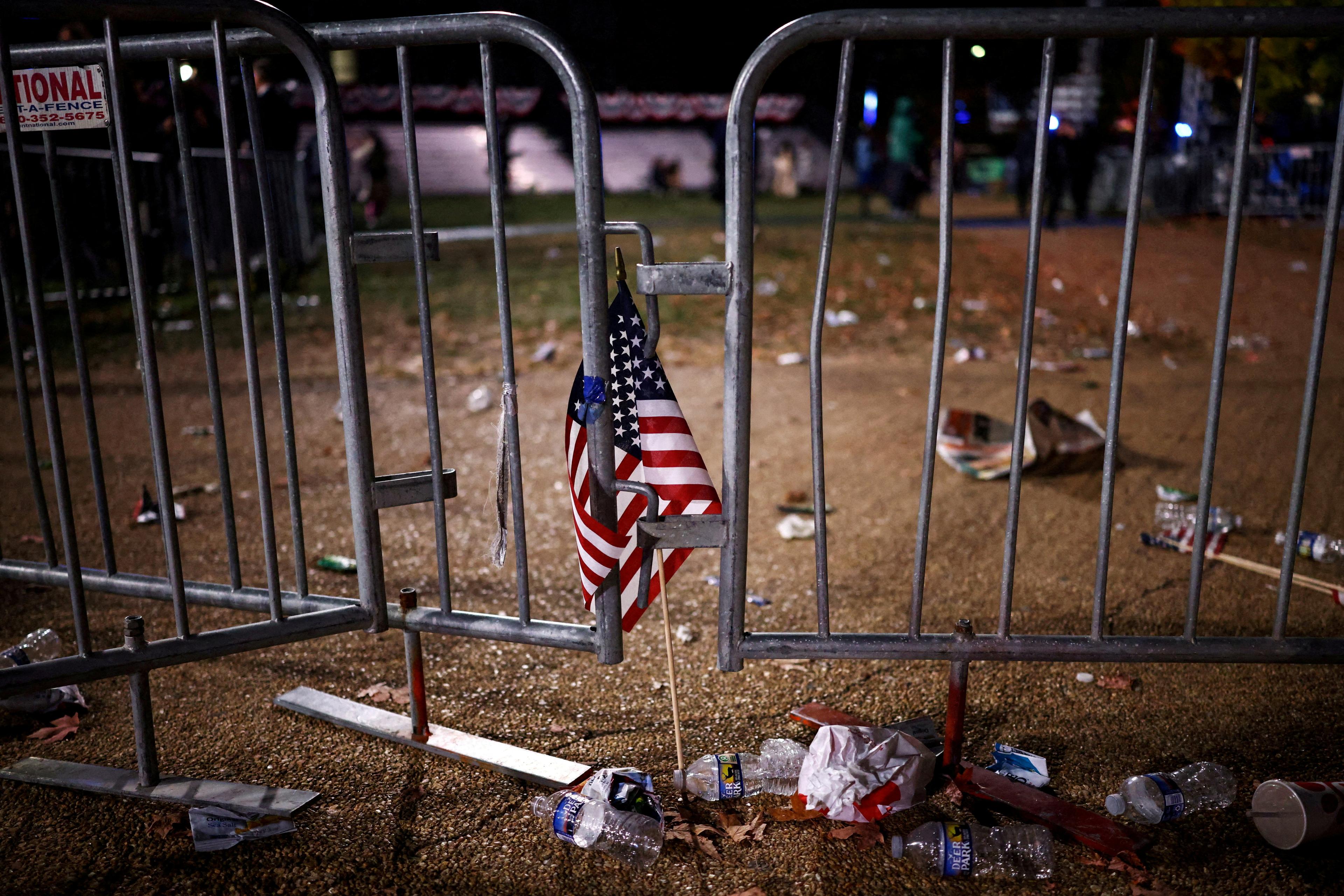 Photo of a small American flag on a metal barrier surrounded by litter at night.