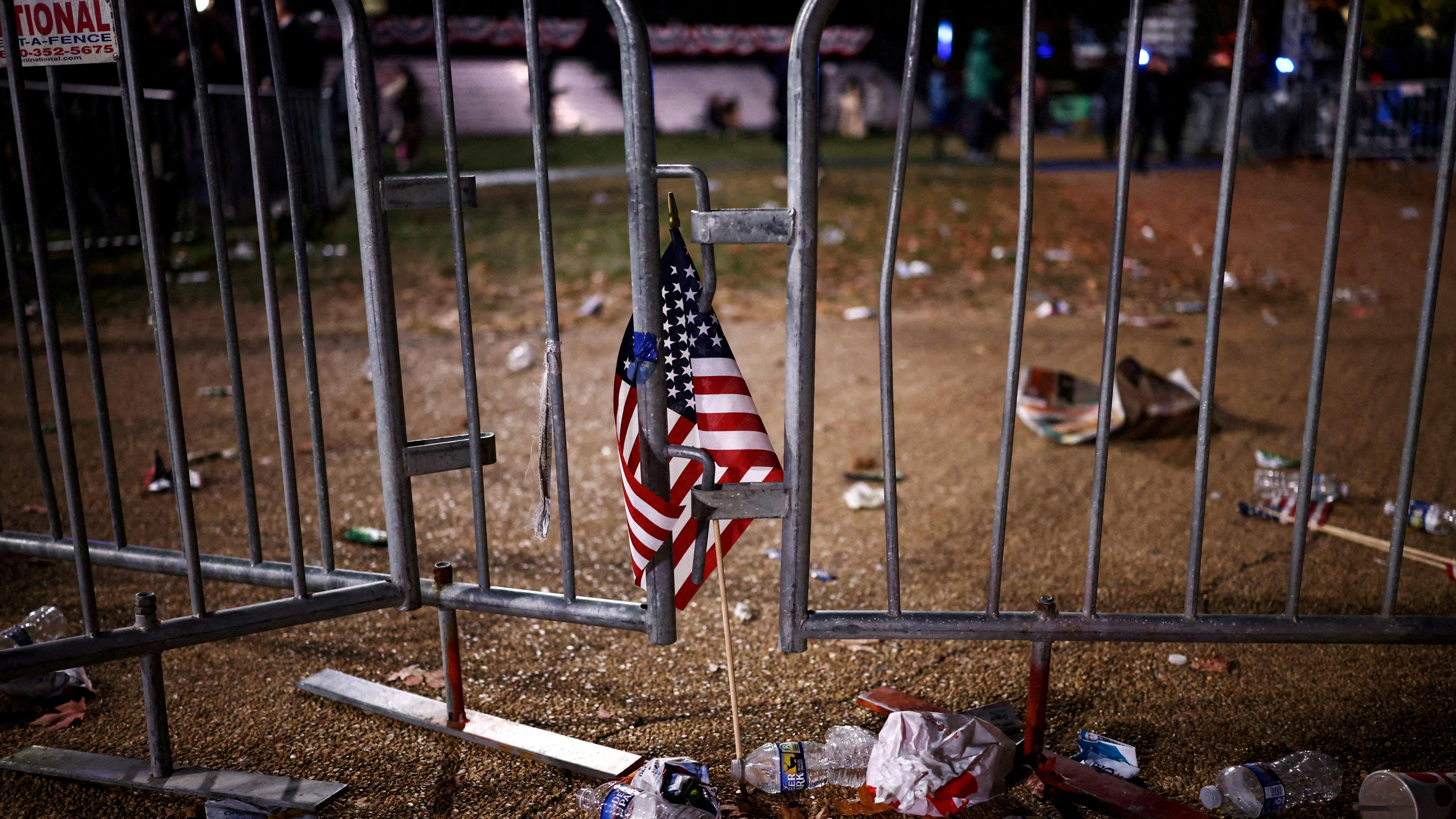 Photo of a small American flag on a metal barrier surrounded by litter at night.