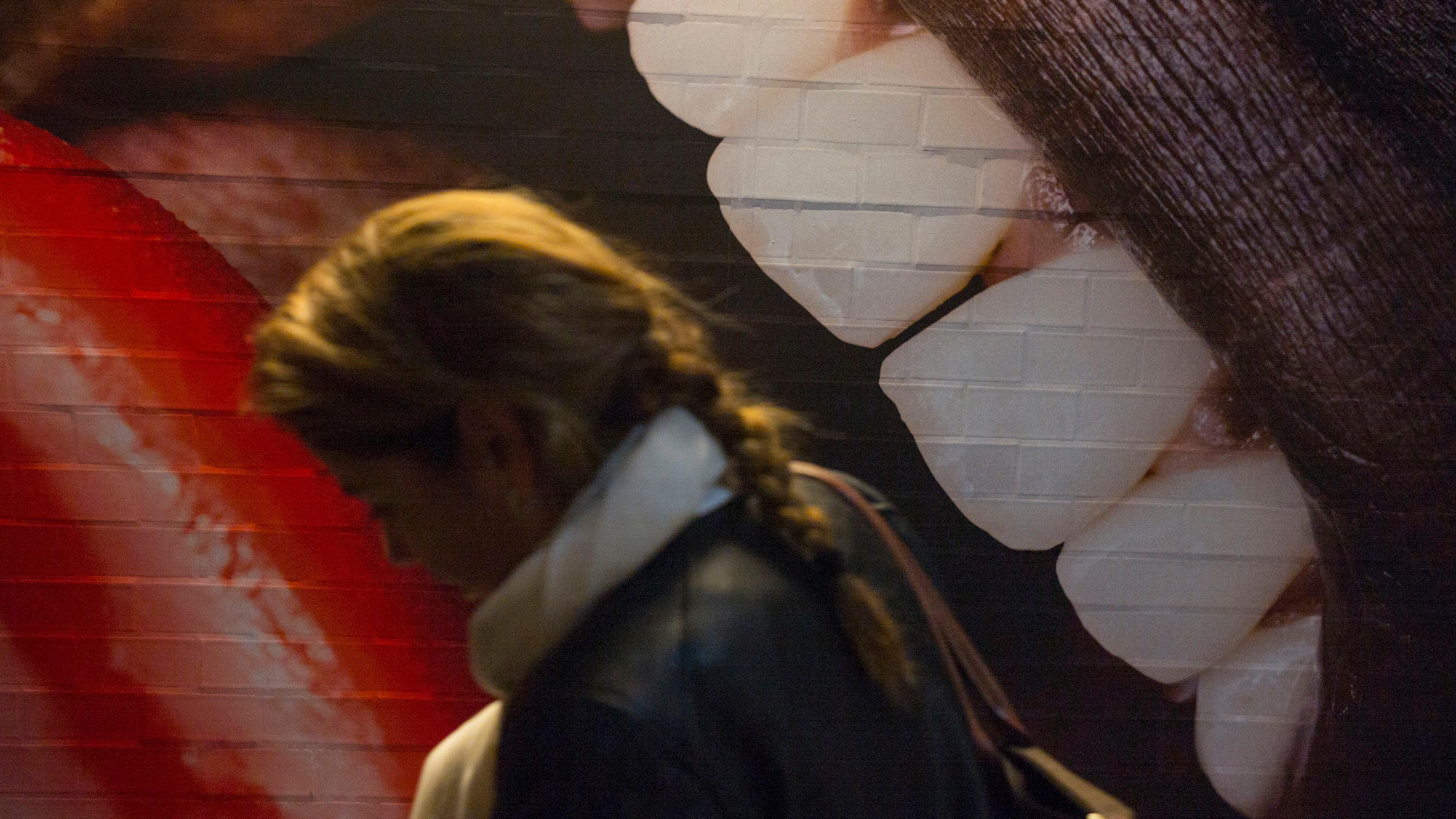 Photo of a woman walking past a mural of large teeth and lips on a brick wall.