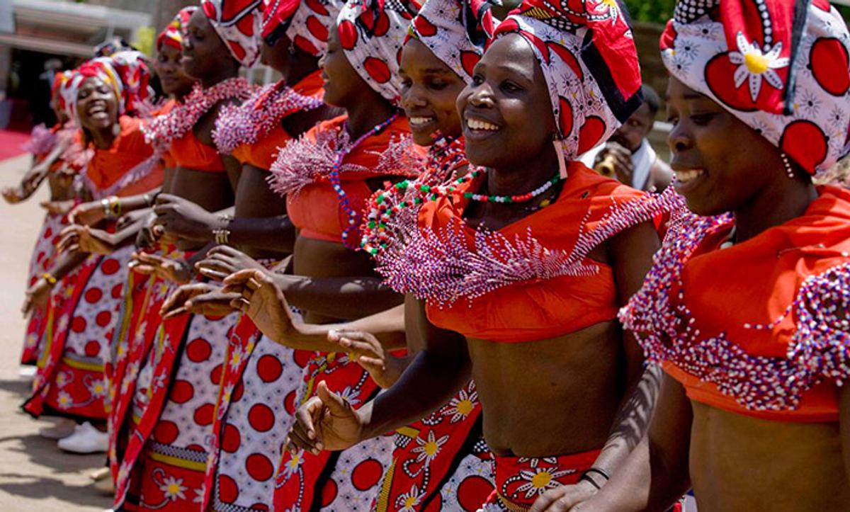 A group of women wearing colourful traditional attire, dancing and smiling as part of a cultural celebration.