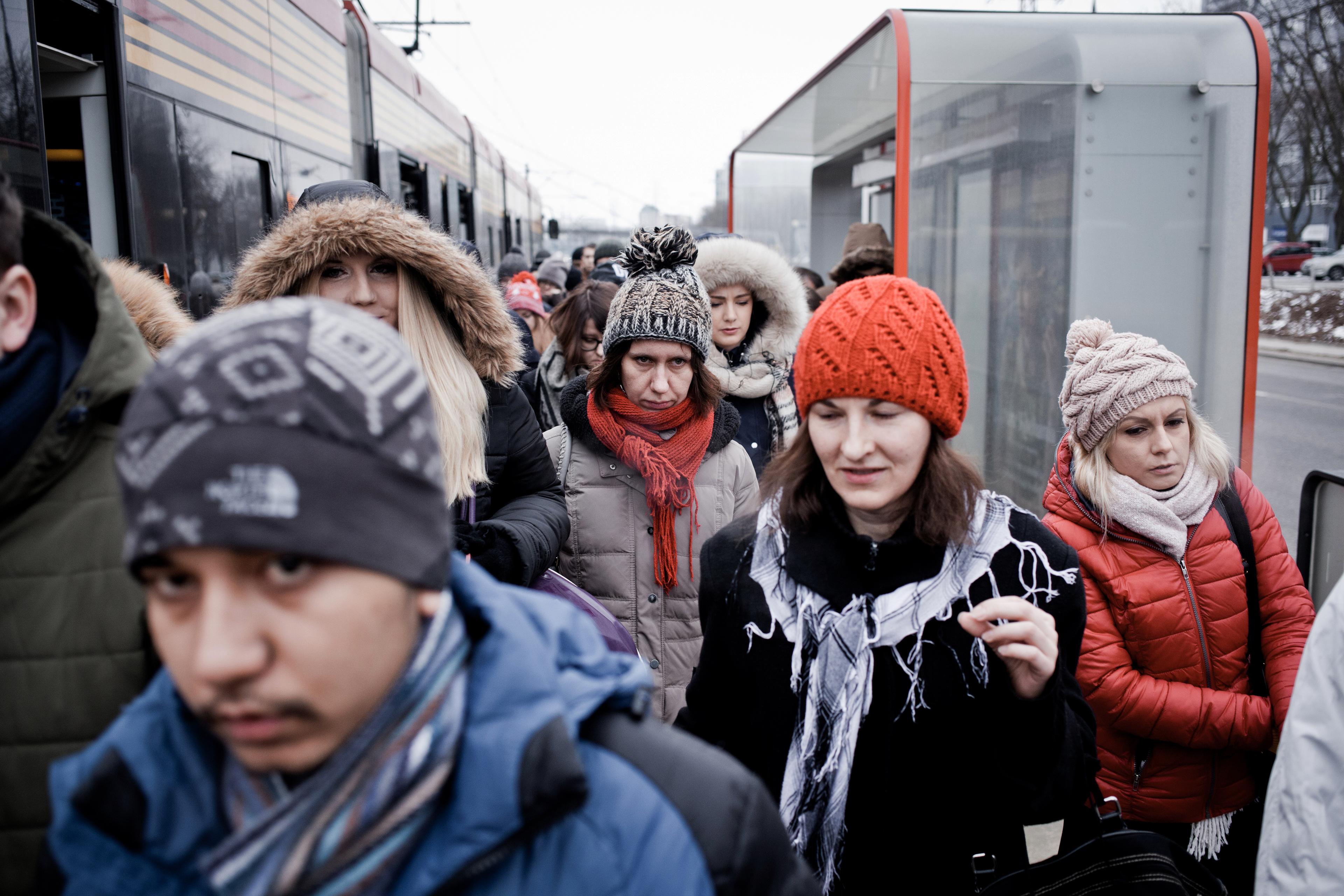Photo of people in winter clothing exiting a tram at a busy station.