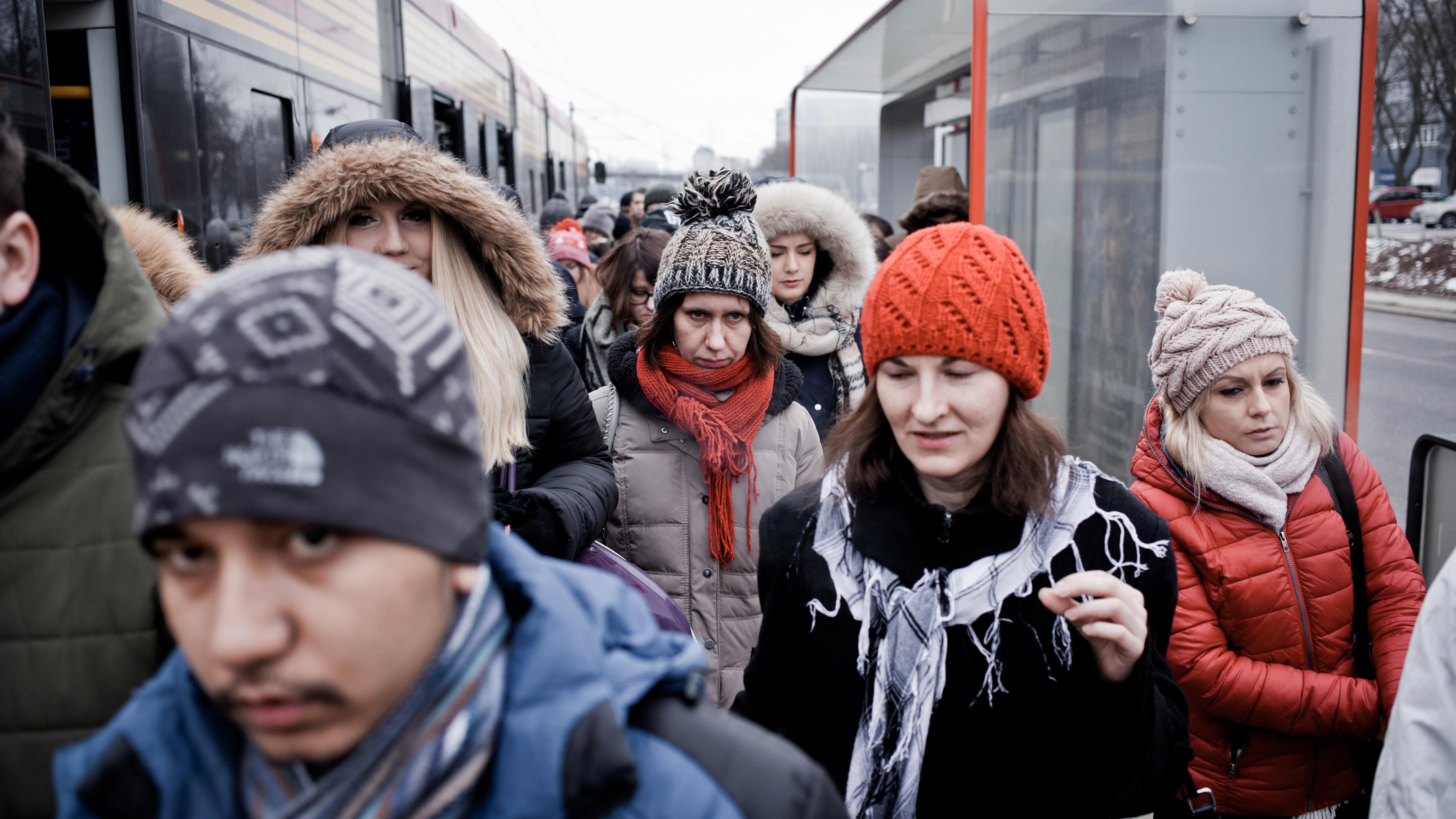 Photo of people in winter clothing exiting a tram at a busy station.