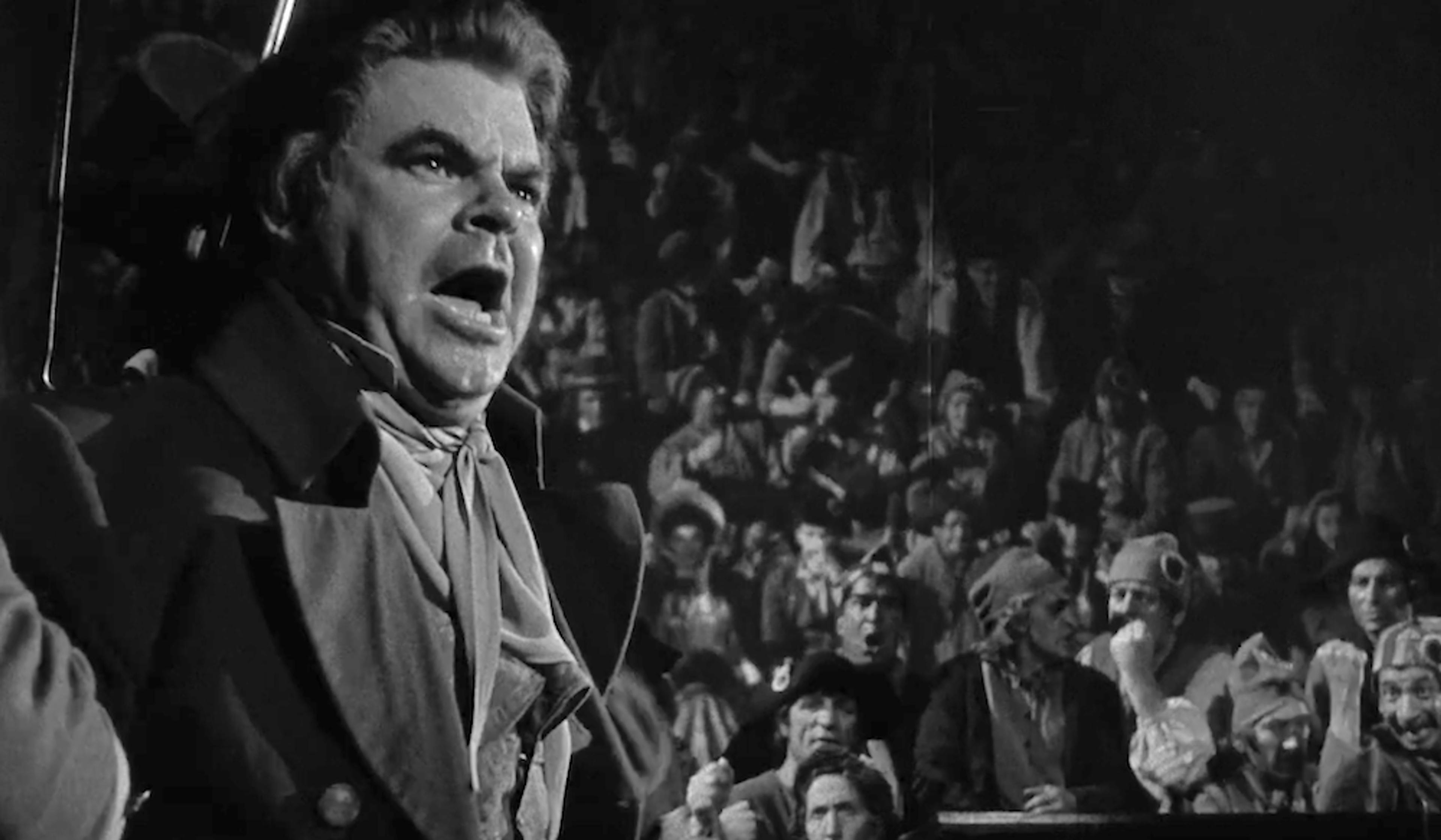 Vintage photo of a man in period clothing shouting passionately with a large audience in the background.