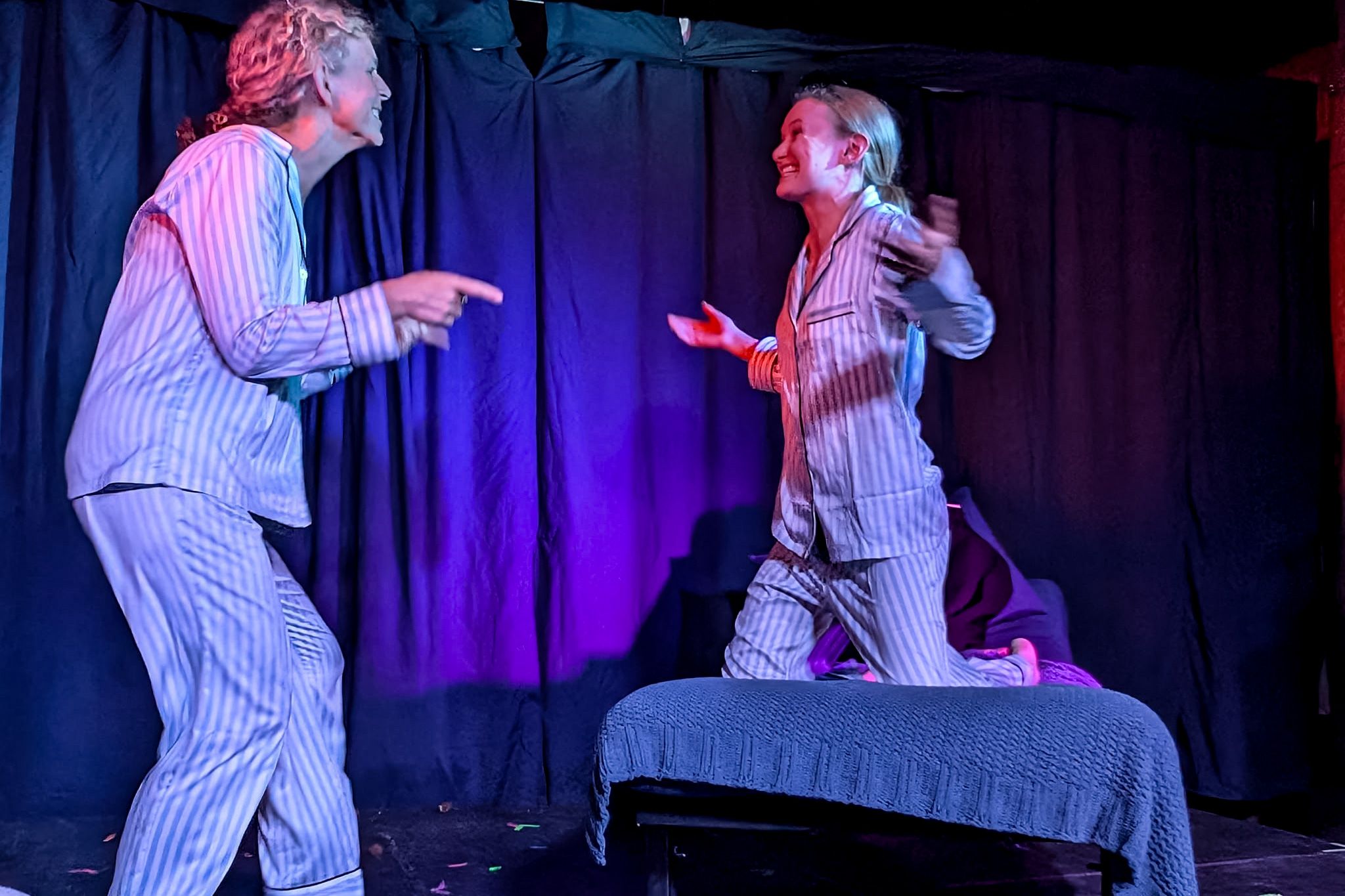 Two people in striped pyjamas acting playfully on stage with dark curtains and blue lighting.