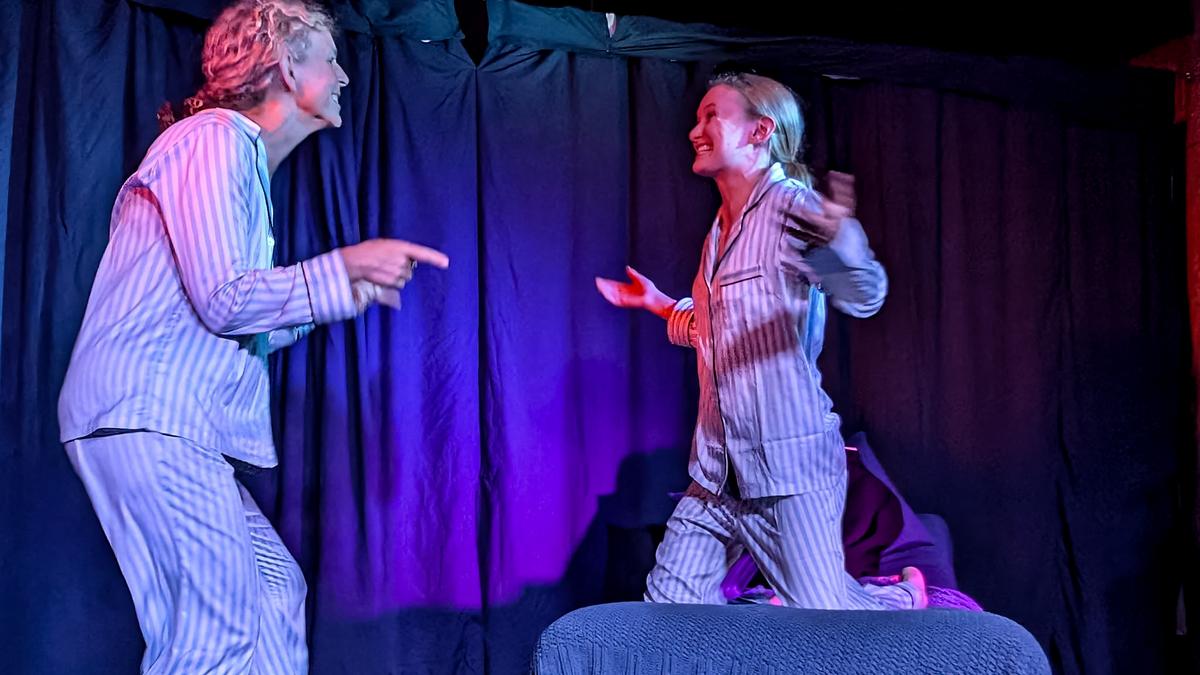 Two people in striped pyjamas acting playfully on stage with dark curtains and blue lighting.