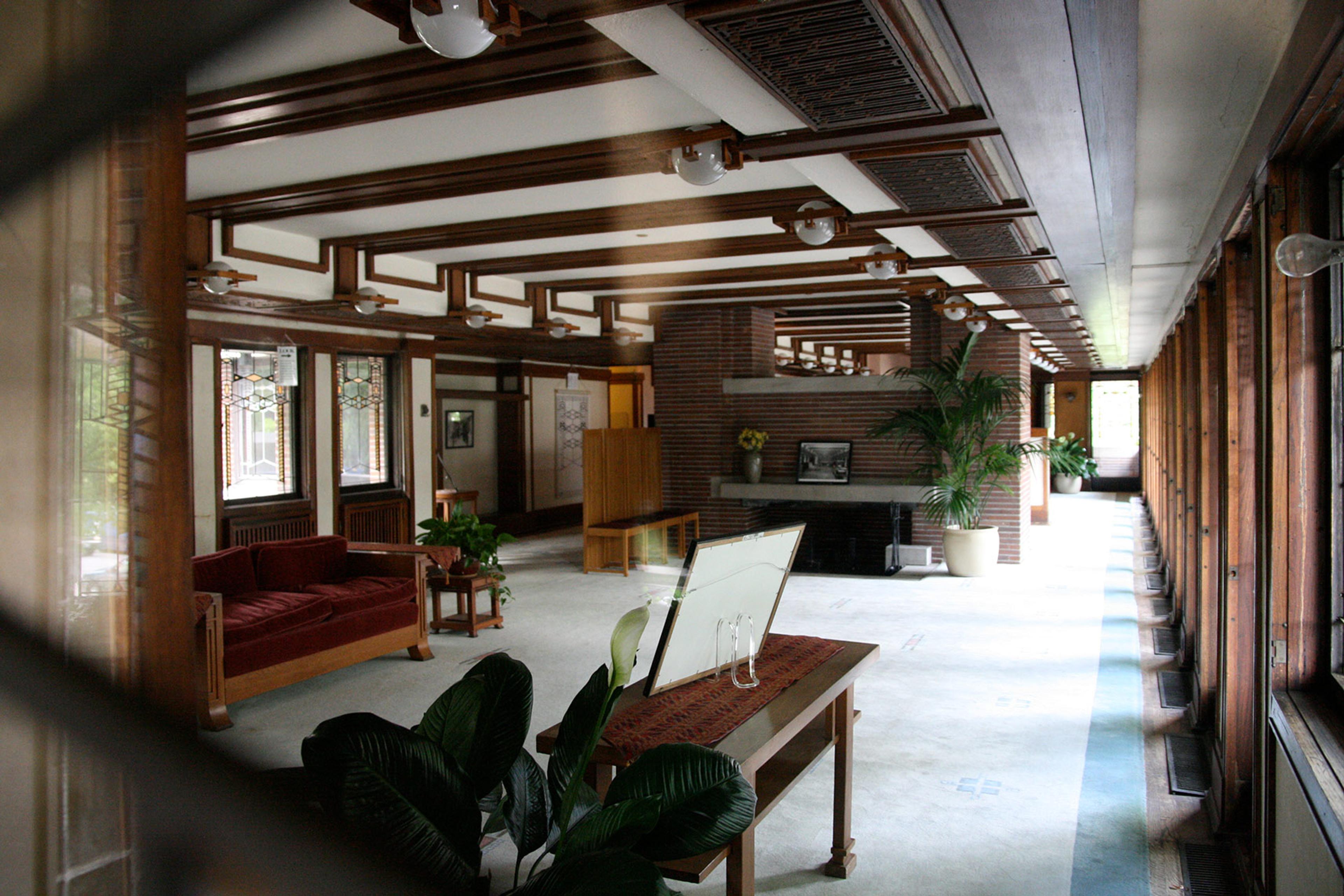 A spacious room with wooden beams, red sofa, plants and large windows letting in natural light.