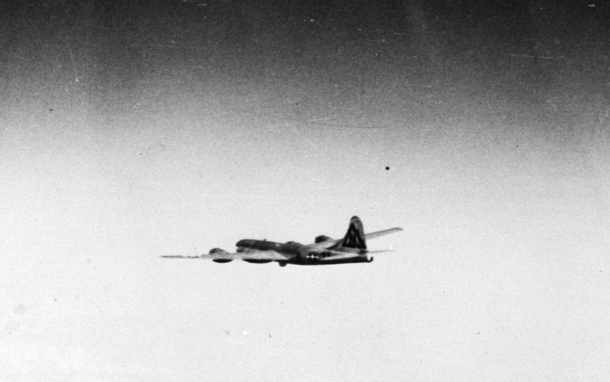 Black and white photo of a vintage propeller aircraft flying in a clear sky.