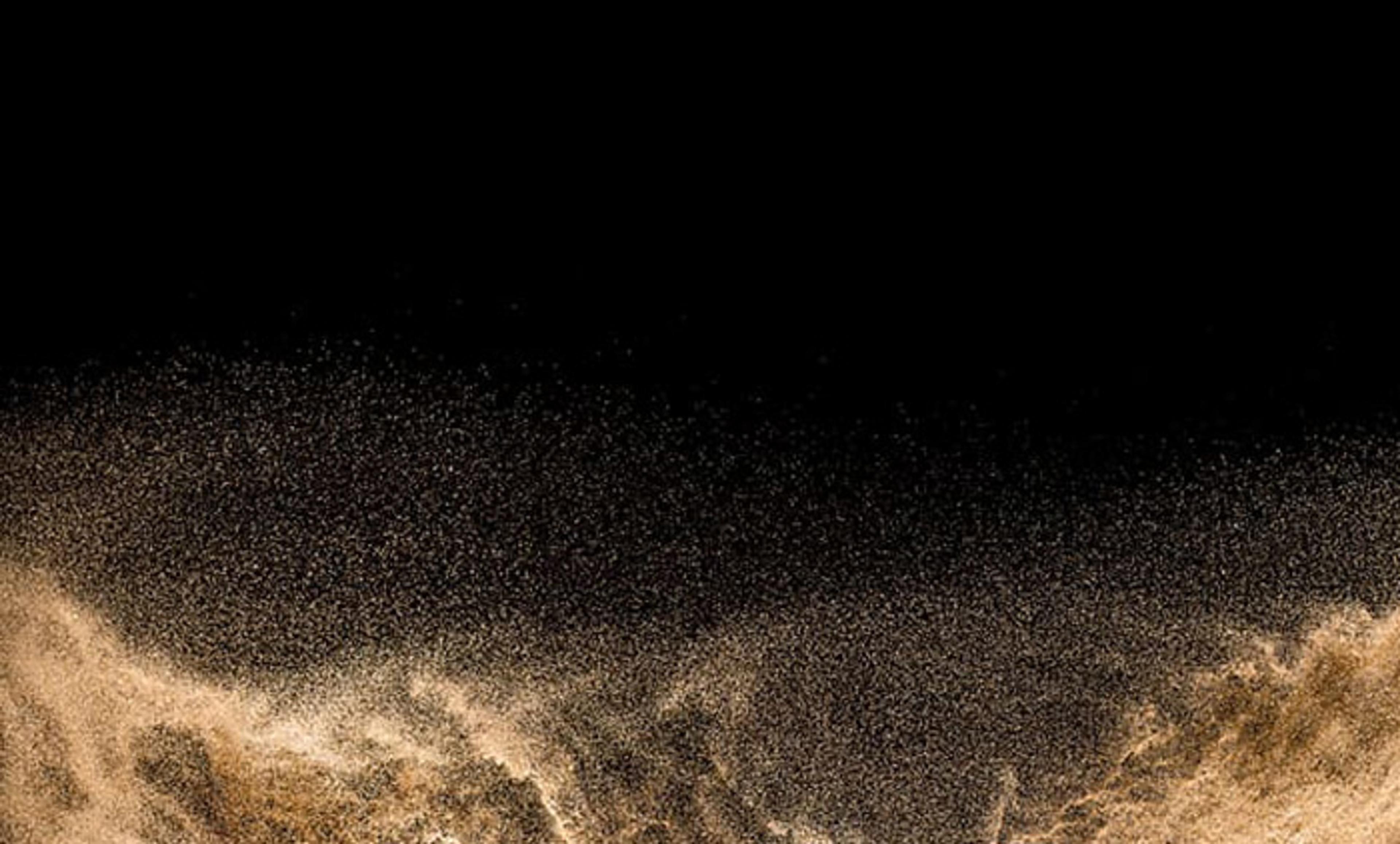 Abstract photo of a cloud of brown sand particles against a black background, creating a dynamic and textured wave-like effect.