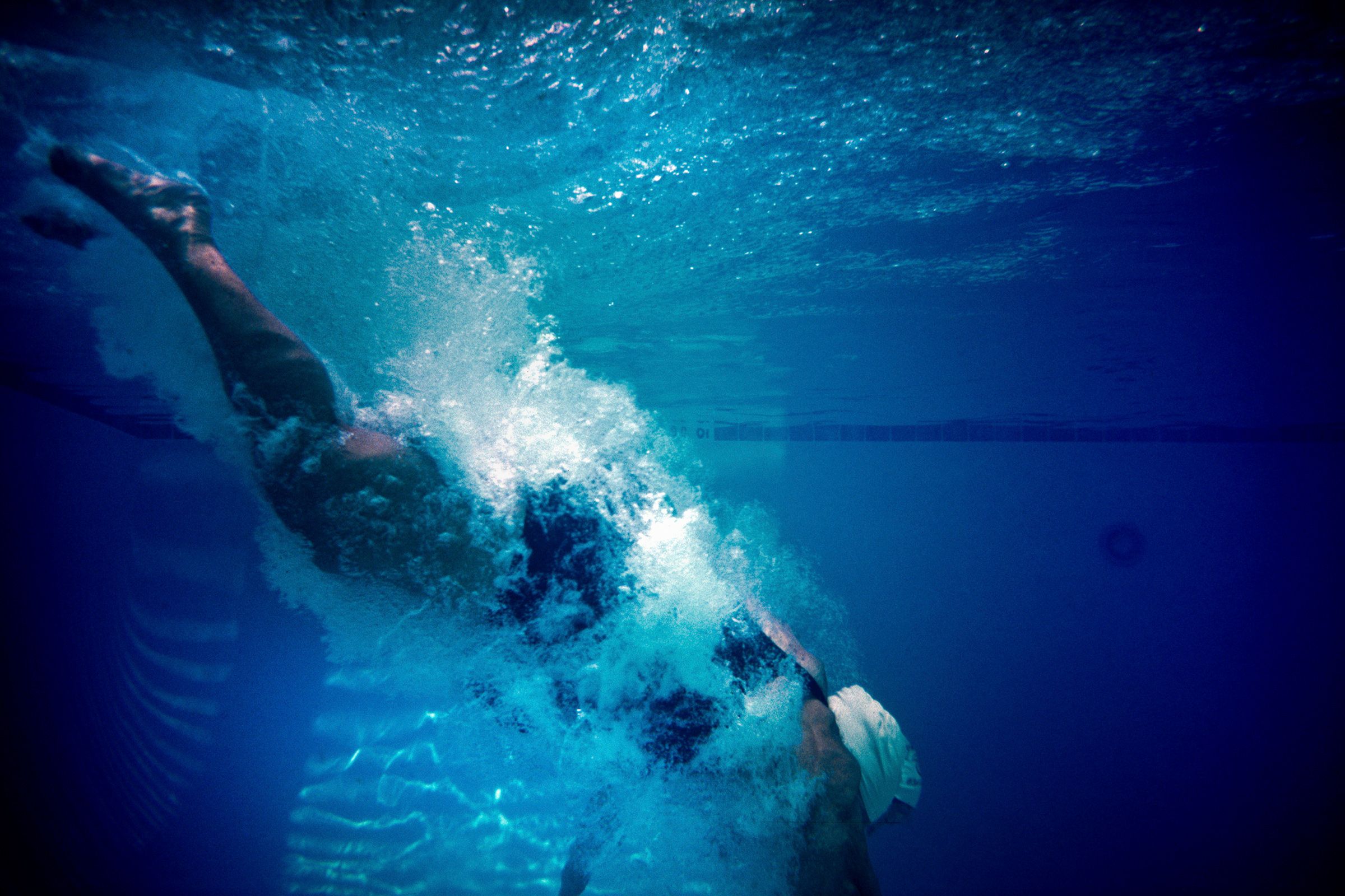 Underwater photo of a swimmer diving into a pool creating a splash against a blue background.