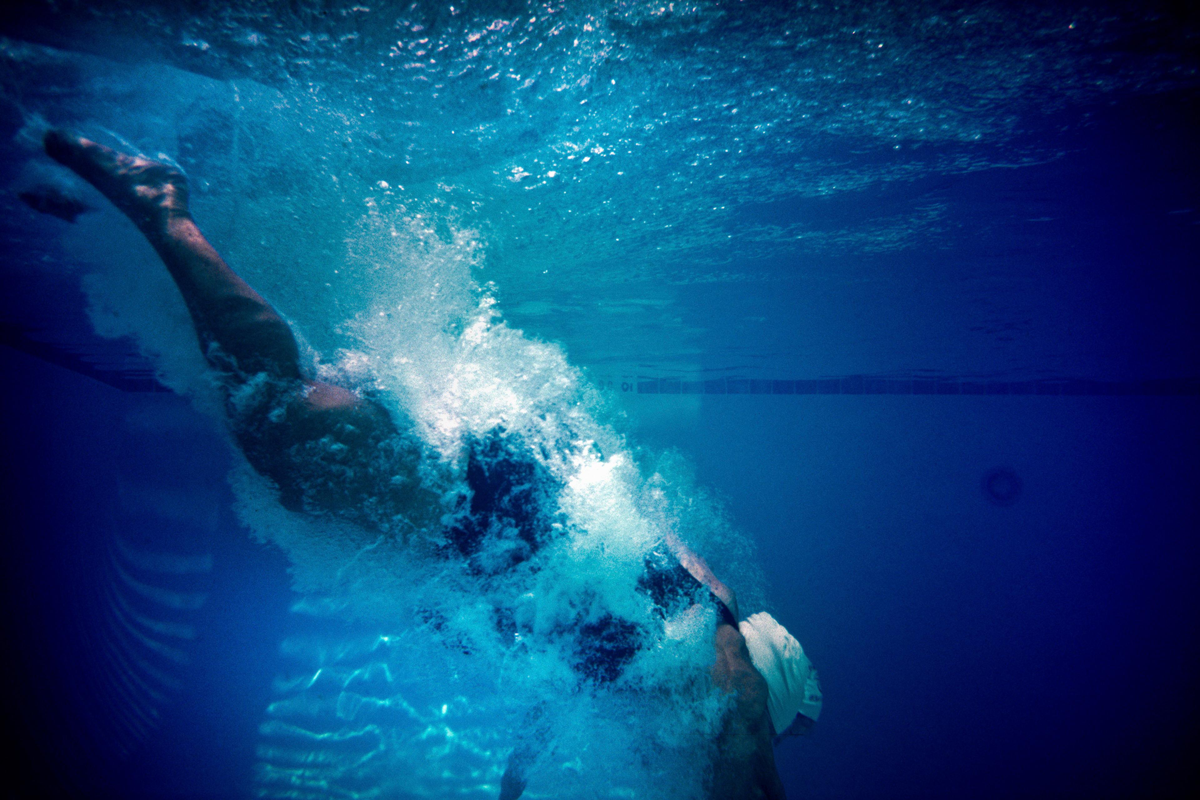 Underwater photo of a swimmer diving into a pool creating a splash against a blue background.